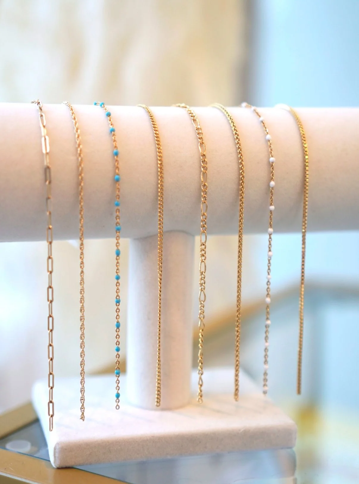 Multiple gold permanent jewelry chains displayed on a white jewelry stand.