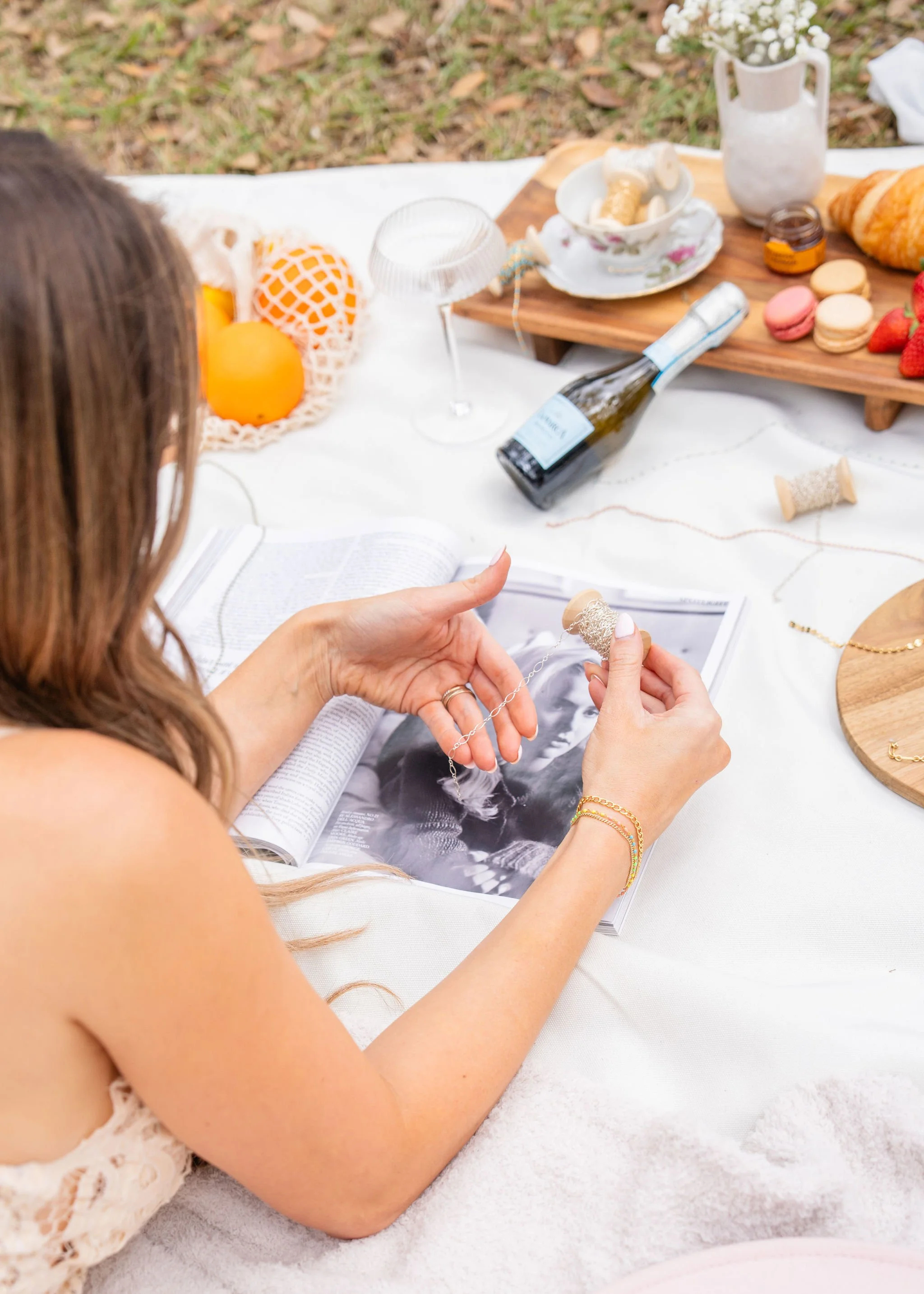 A women at a pop up jewelry event, a bottle of champagne near by. Looking at permanent jewelry chains. Deciding which bracelet she will choose as her hostess gift.