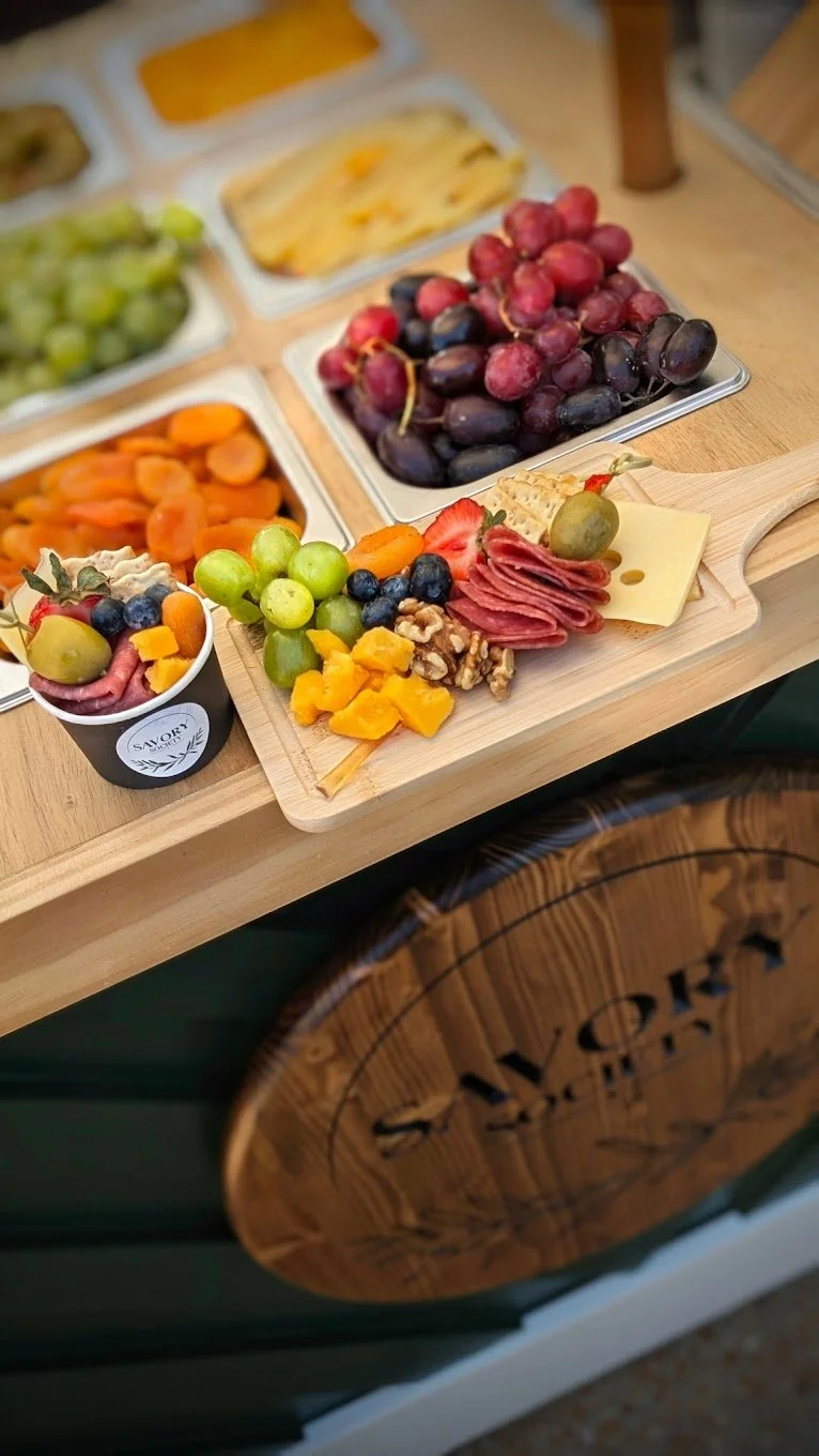 Assorted fresh fruits, cheese, and charcuterie on a wooden serving board on a mobile charcuterie cart.
