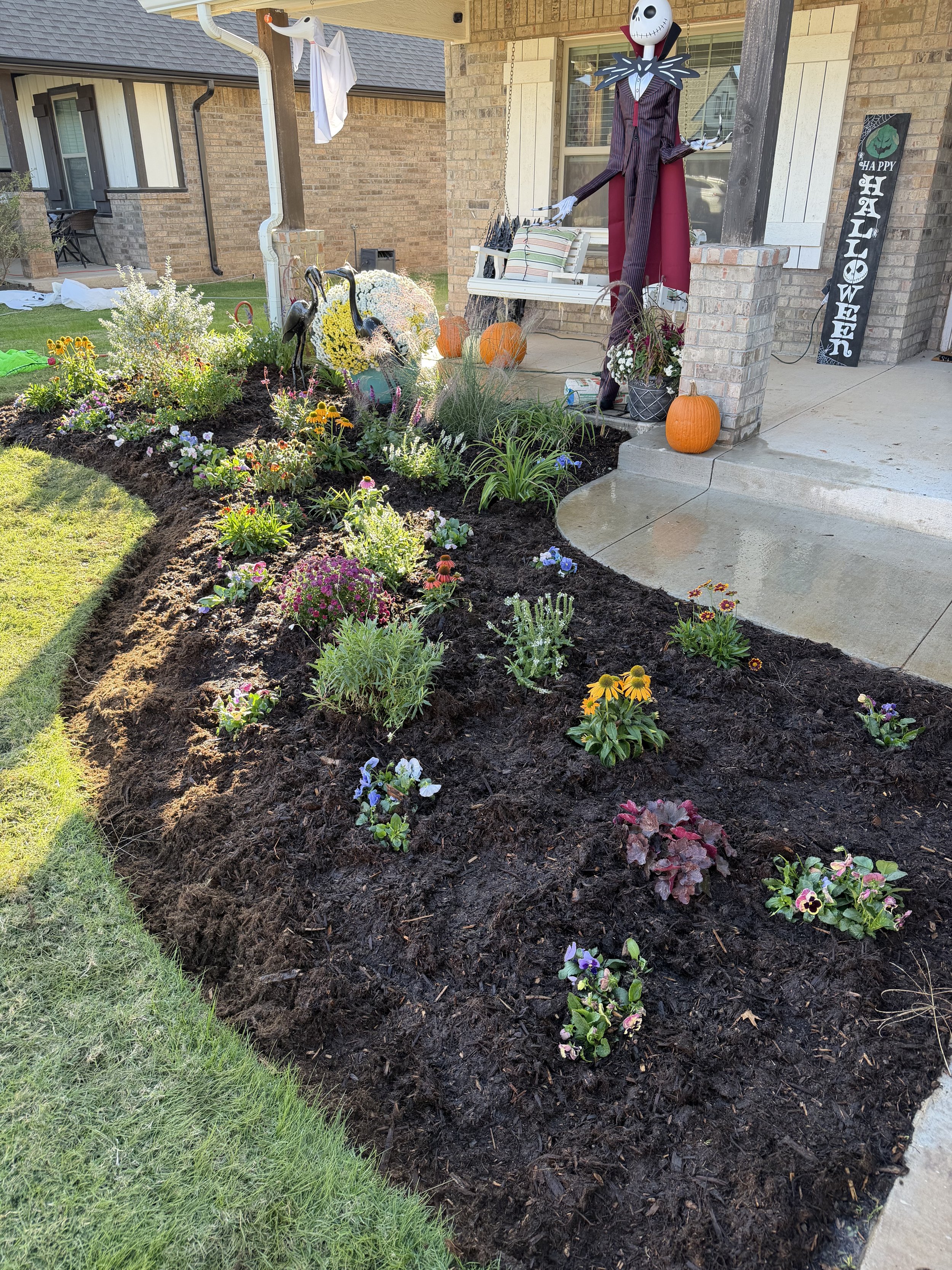 Front yard garden with various flowers, Halloween decorations including a large skeleton figure, pumpkins, and a 'Happy Halloween' sign.