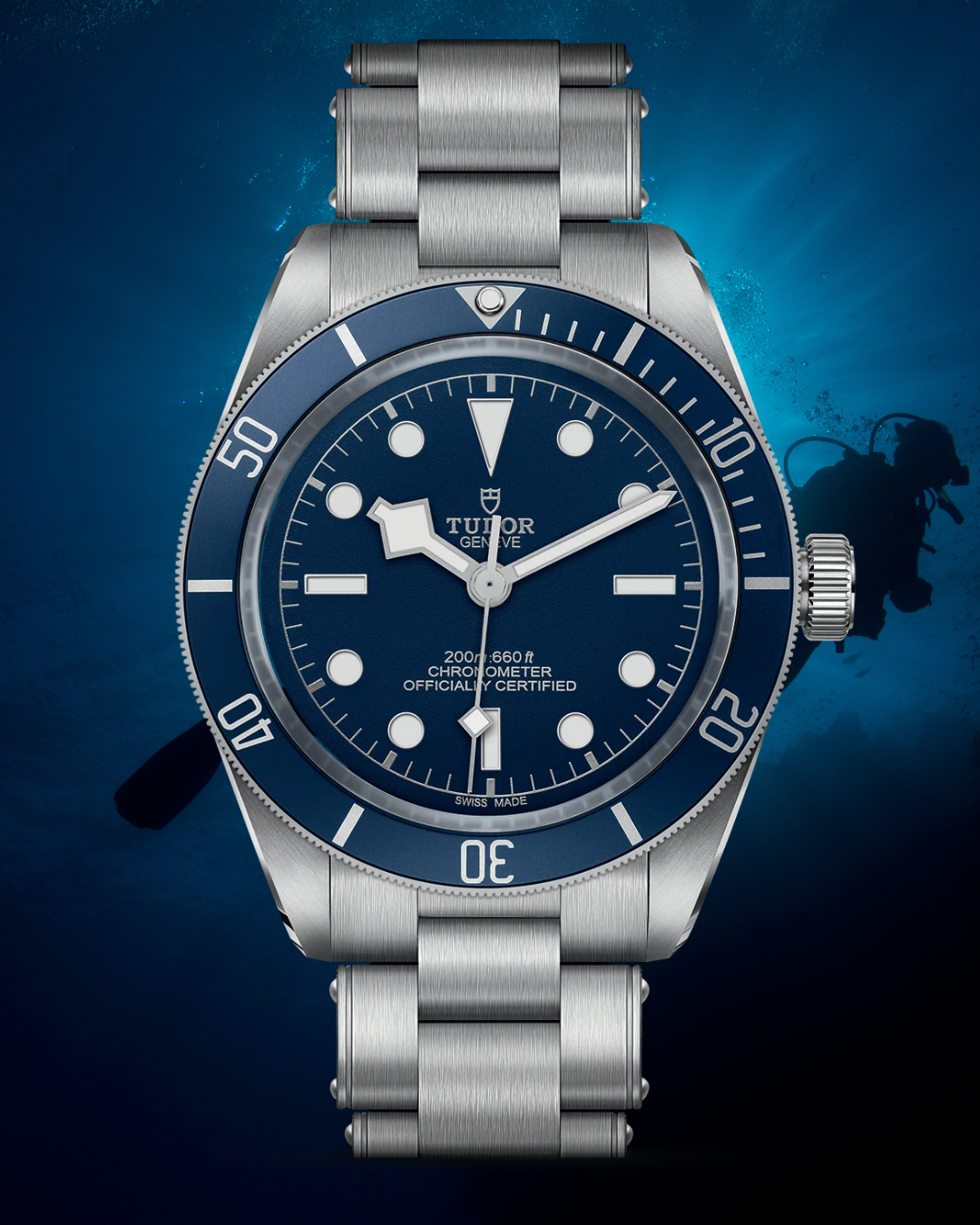 A Tudor dive watch with a blue dial and bezel, featuring a stainless steel bracelet, set against an underwater background with a scuba diver silhouette.