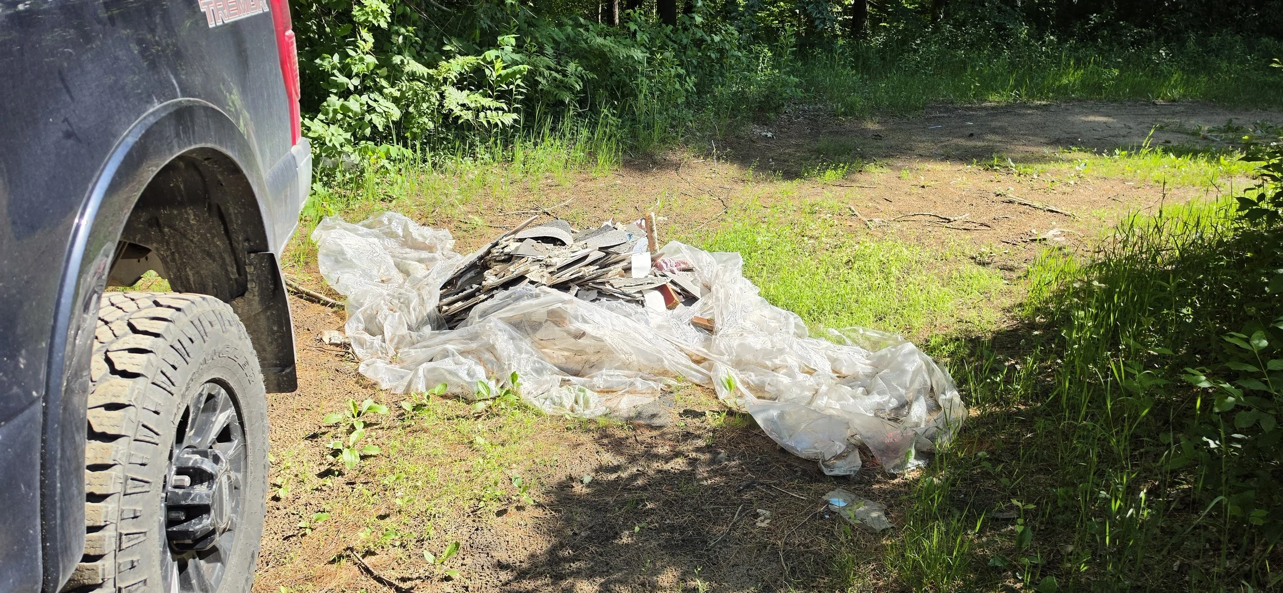 Plastic and construction debris illegally dumped in a parking area of a Michigan State Game Area, highlighting the need for public land stewardship.