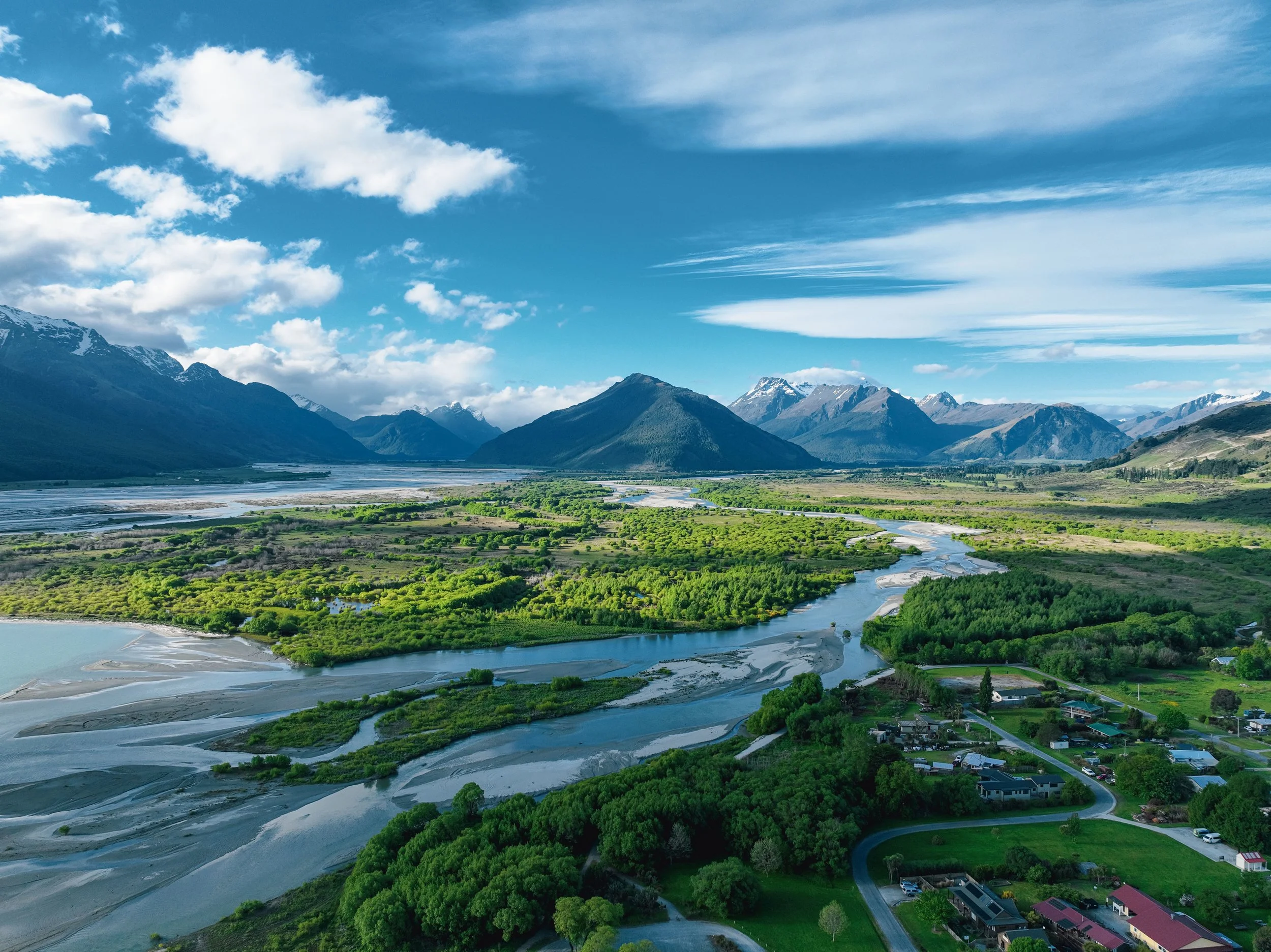 A scenic valley with a winding river, lush green trees, and mountains in the background under a partly cloudy sky.
