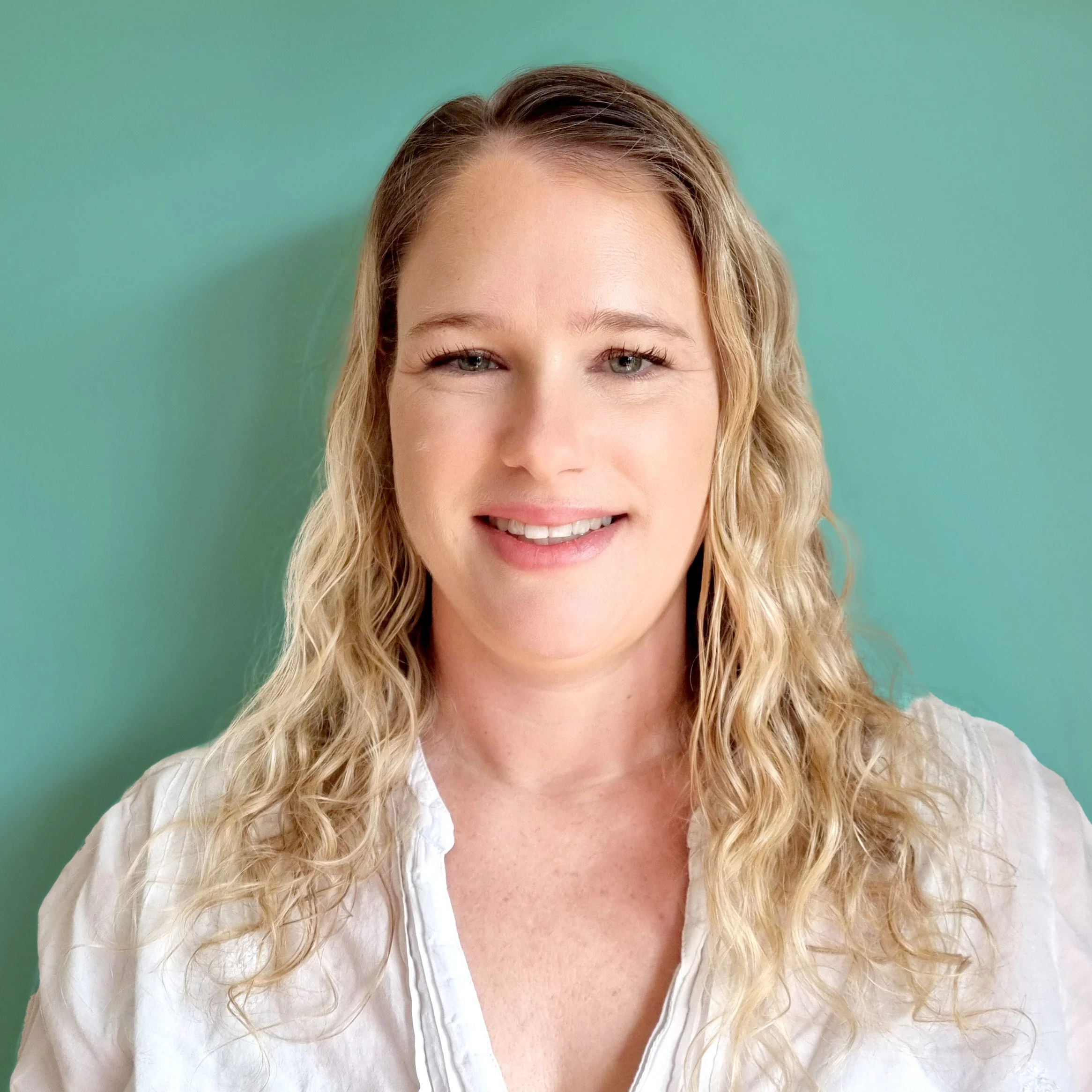 Portrait of a young woman with blonde, curly hair smiling against a teal background.