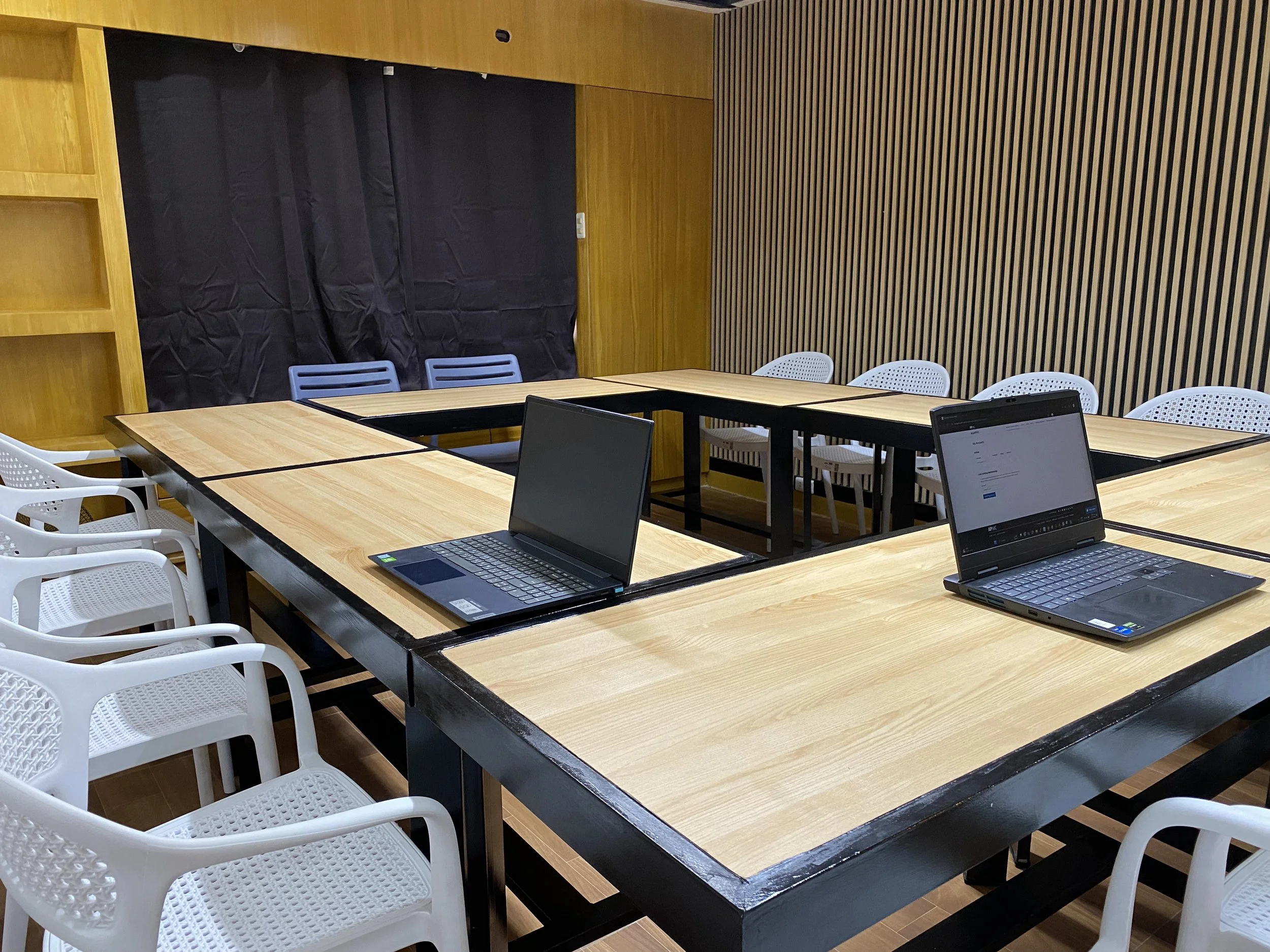 A conference room with a U-shaped wooden table, two laptops open on the table, and white and blue chairs around the table.