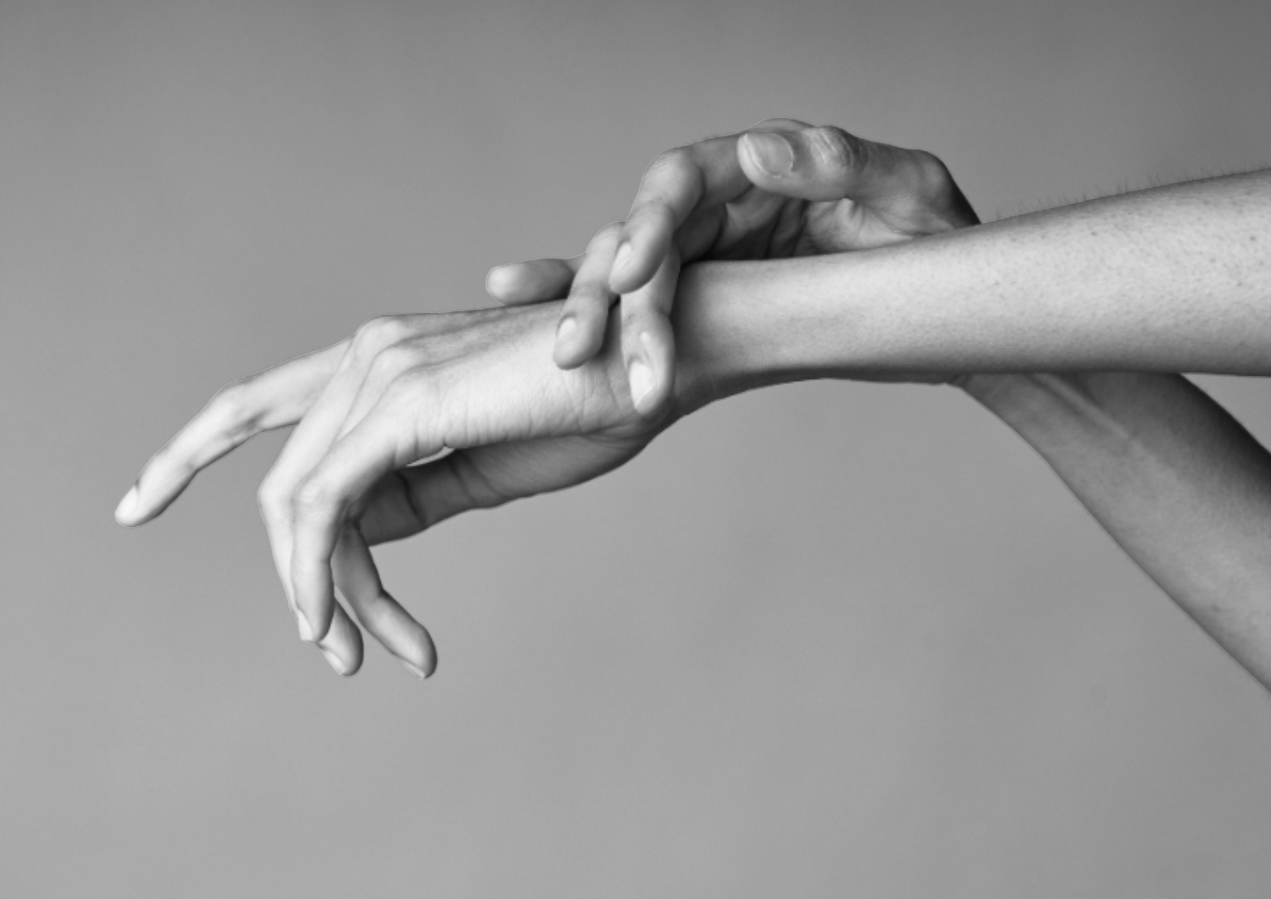 Black and white photo of two hands touching, with one hand gently resting on the other's wrist and the fingers of the resting hand slightly curled.