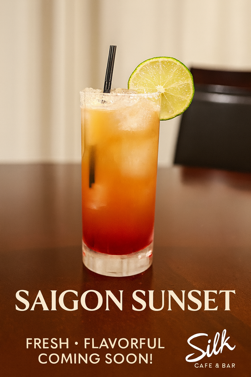 A tall cocktail glass with a layered red and orange drink, garnished with a lime slice and a black straw, on a wooden table.