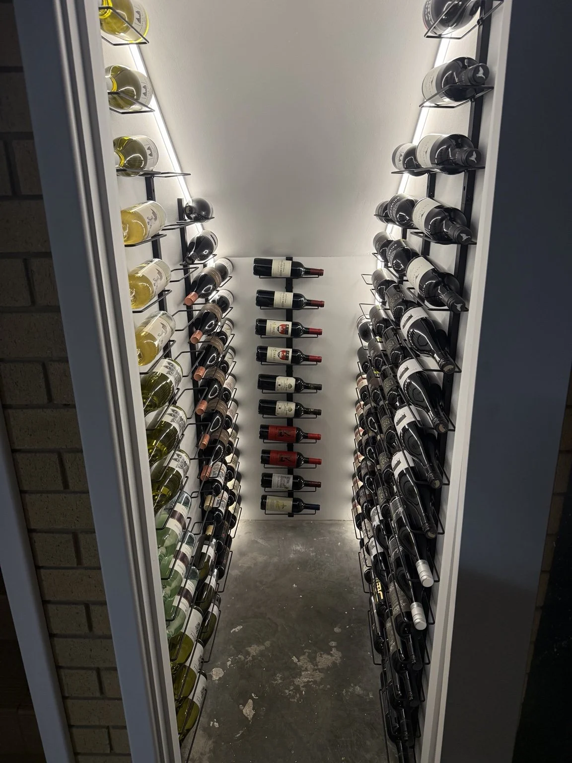 A wine rack displaying multiple bottles of wine on each side, with a variety of red and white wines organized horizontally and with some bottles stored on angled racks for easy access.