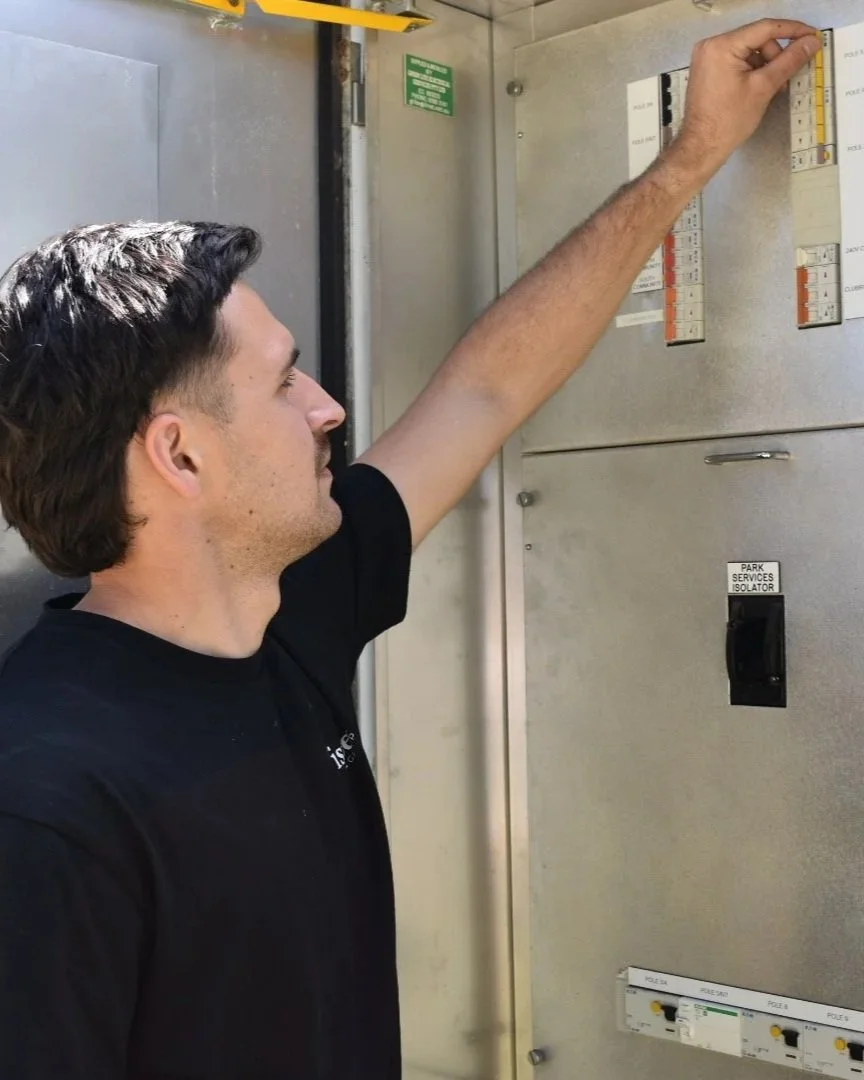 A man with dark hair working on an electrical panel or breaker box, adjusting one of the switches or circuit breakers.