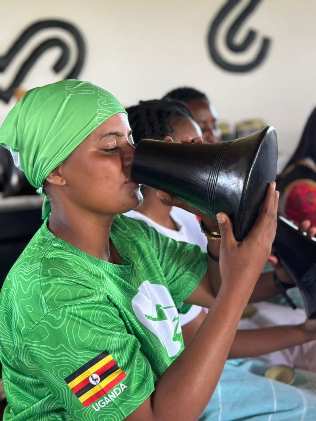 A powerful image capturing a woman drinking traditional Ekyanzi (milk in a carved wooden gourd) in Ankole culture. The intricate pattern on her sleeve shows the Ugandan flag, highlighting the rich heritage that will be celebrated at The Banyankore Kw