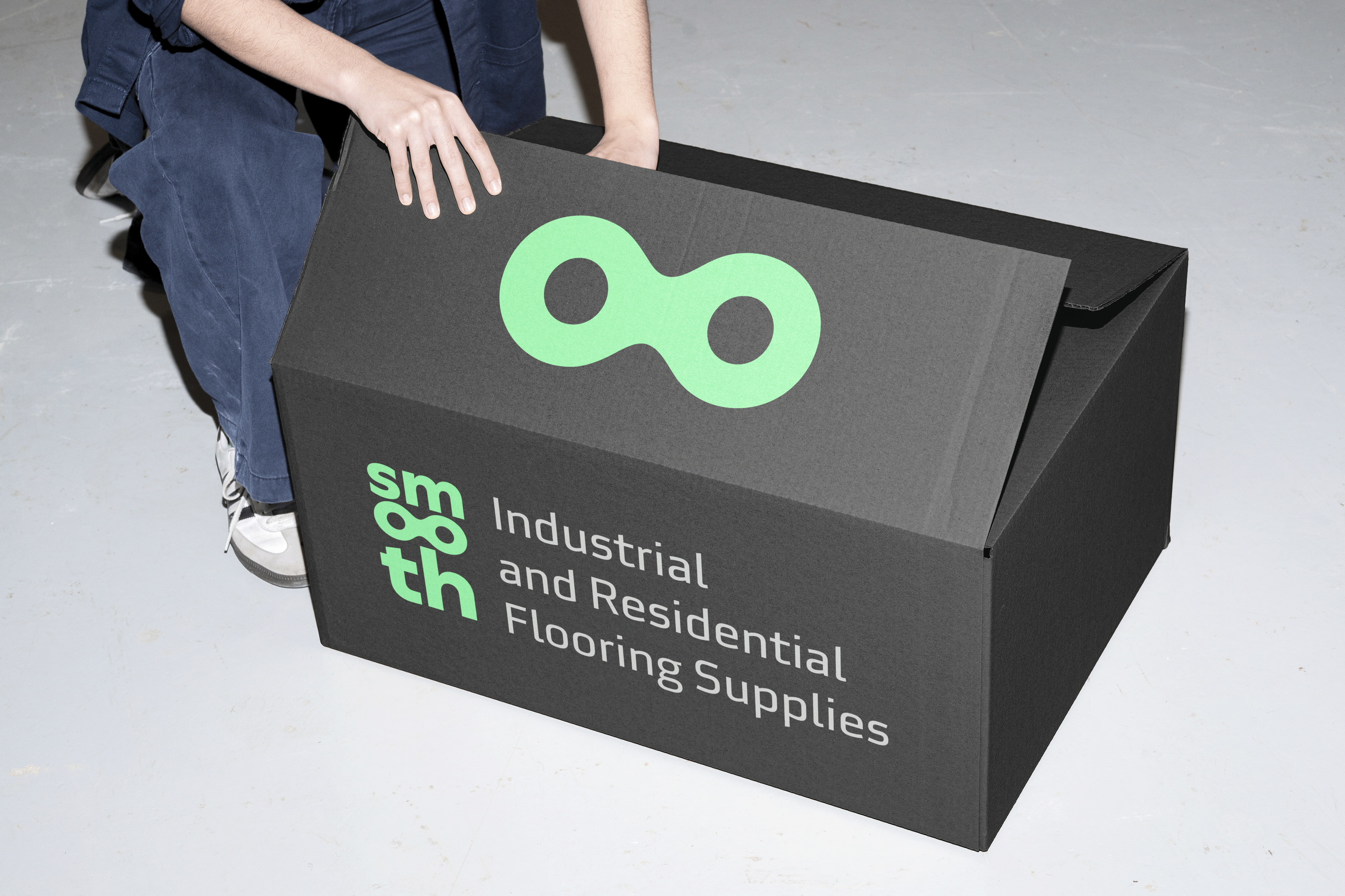 Person opening a black box with green and white text that reads 'th96 Industrial and Residential Flooring Supplies'.