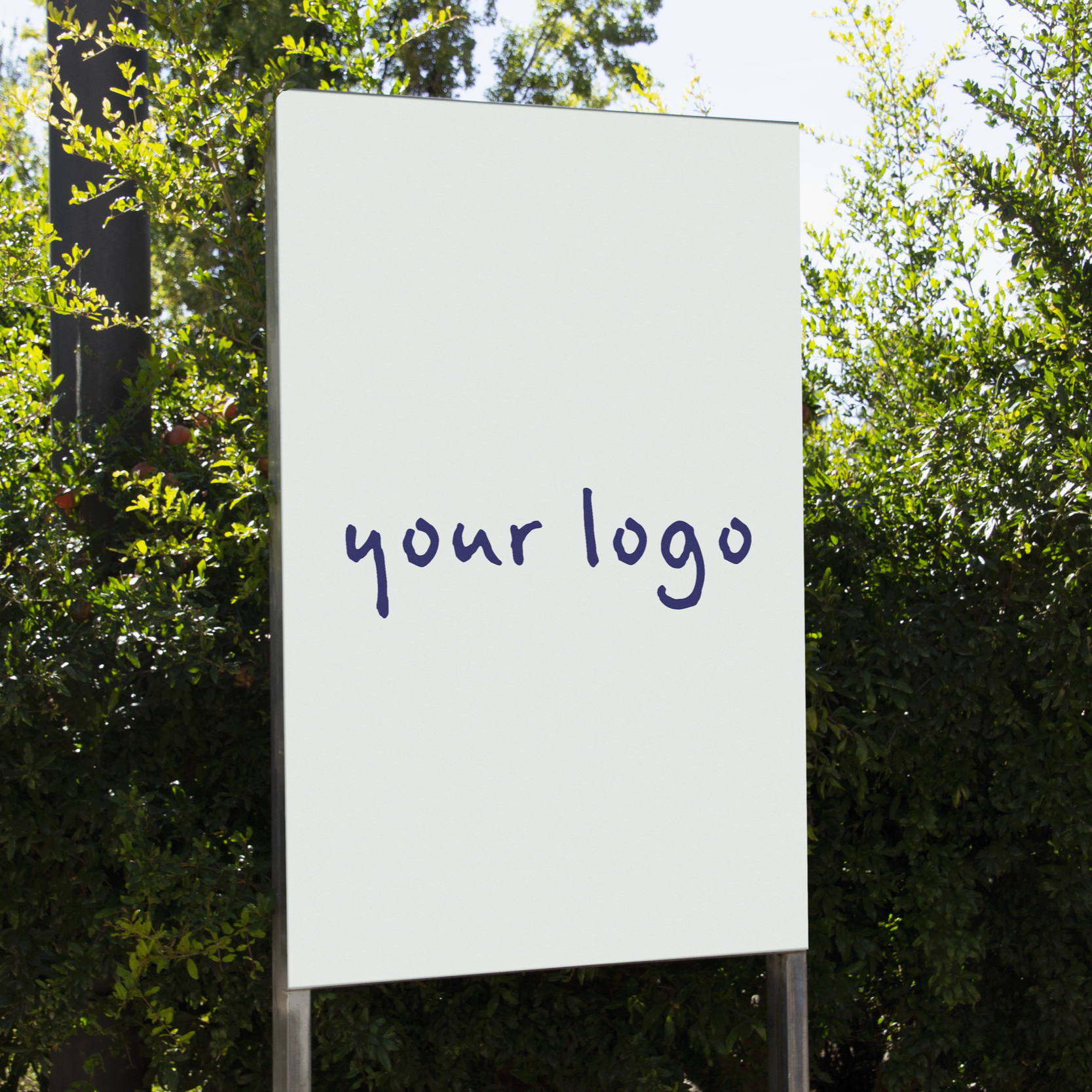 Blank outdoor signboard with the words 'your logo' written in purple handwritten font, surrounded by green trees and shrubs on a sunny day.