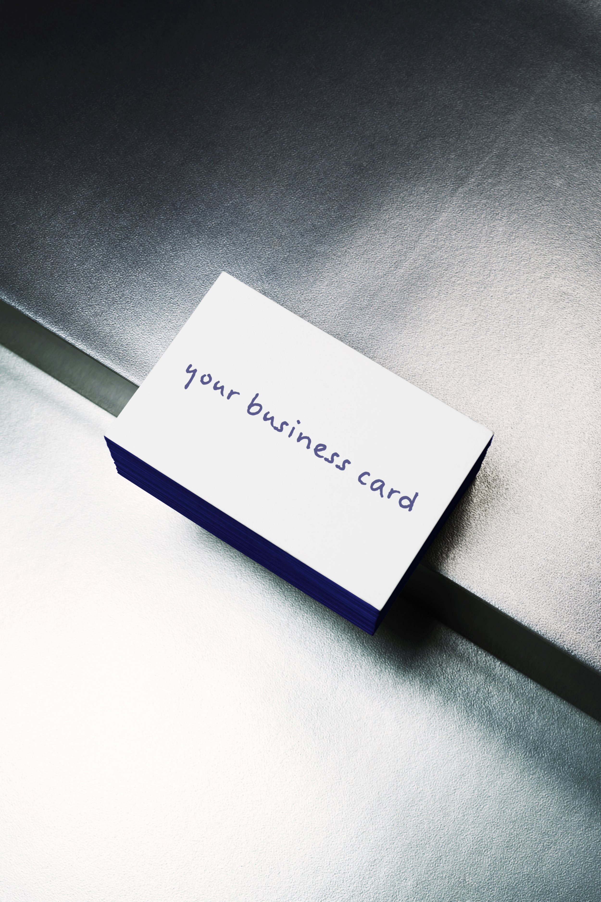 A stack of business cards with handwritten text that reads 'your business card' on top of a metallic surface.