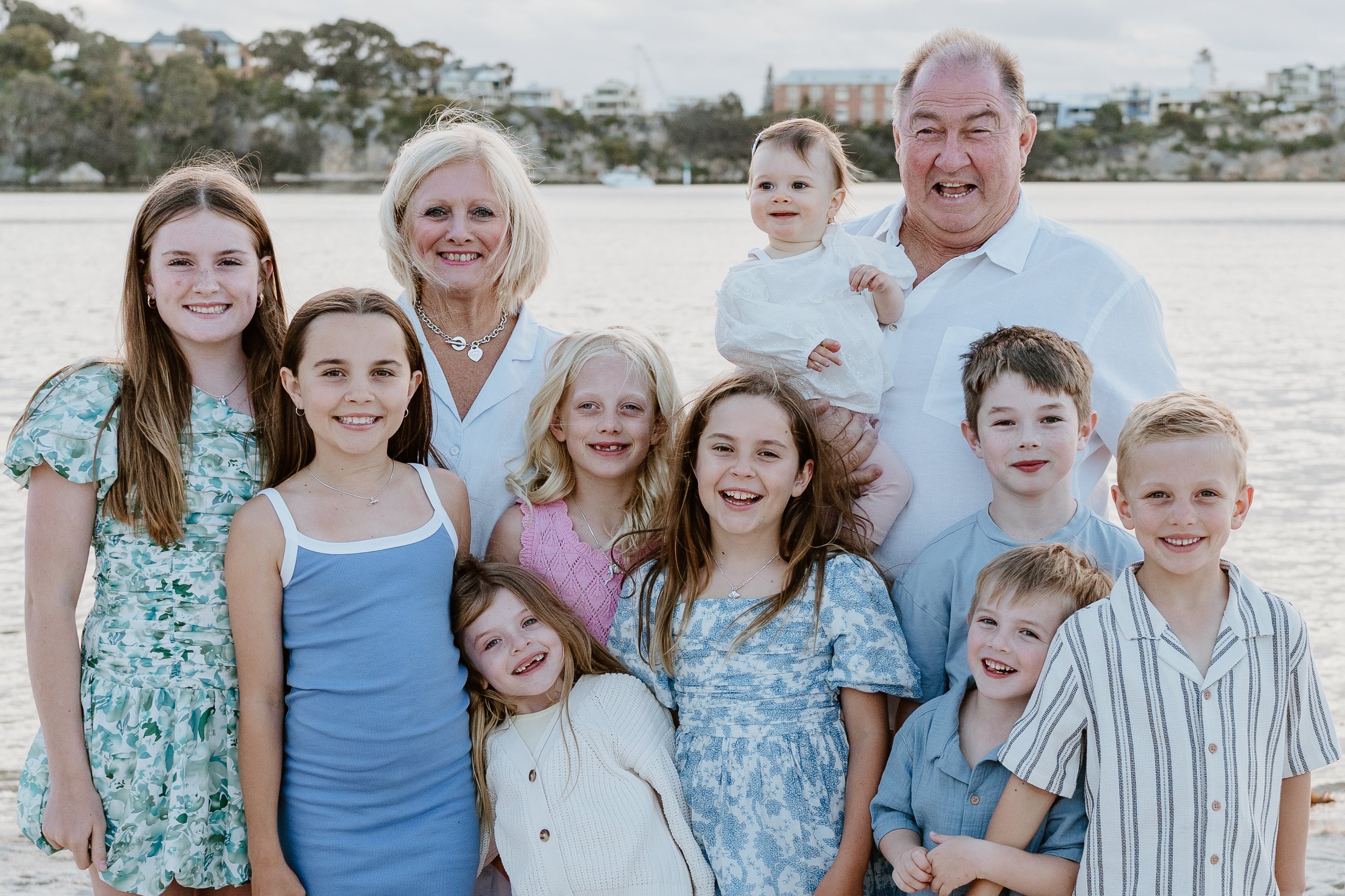 Family of twelve posing outdoors on a beach, with seven children and two older adults, smiling.