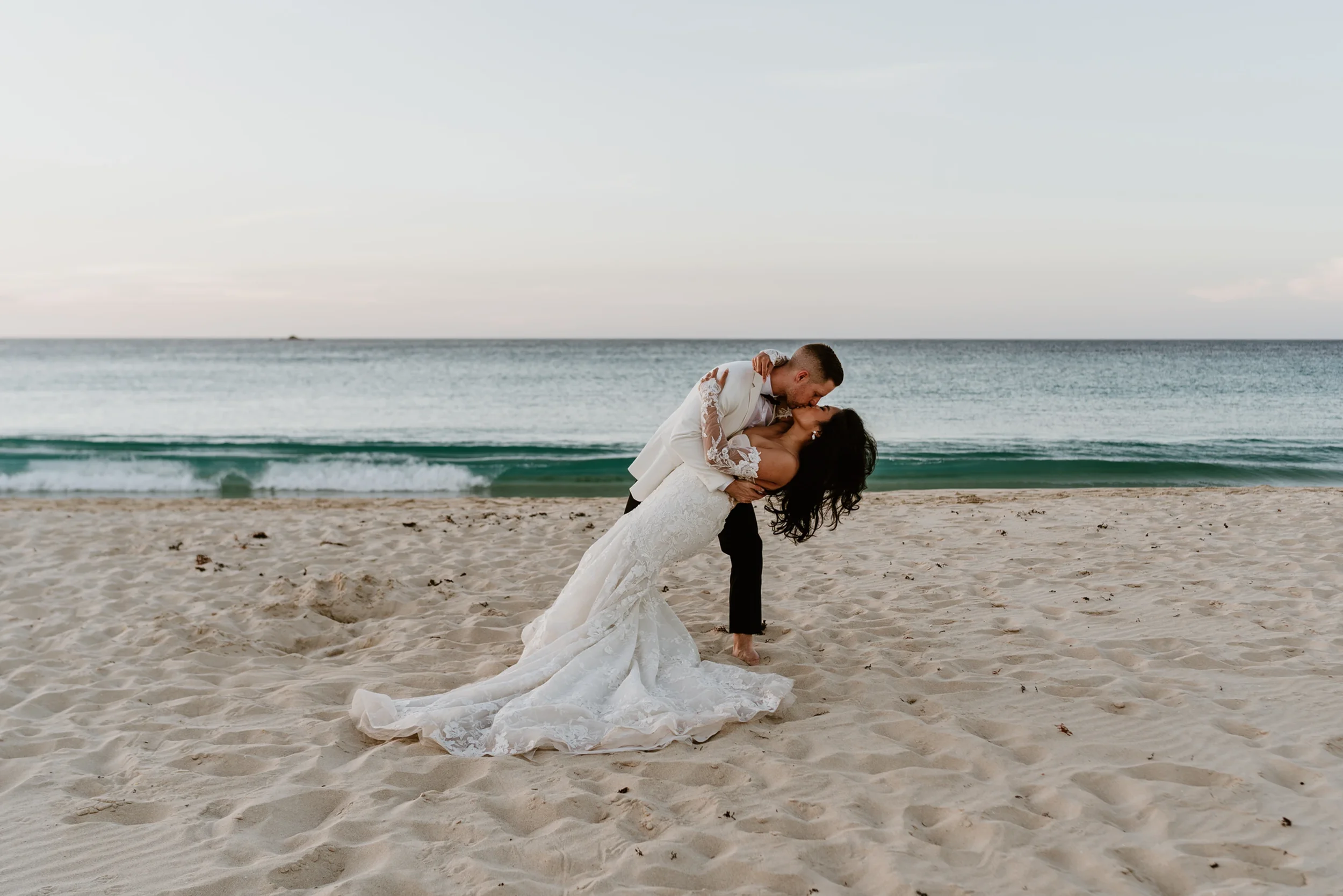 Kristelle and Joel share a special and stunning kiss on their wedding day along the Yallingup coastline with waves crashing behind them just after sunset