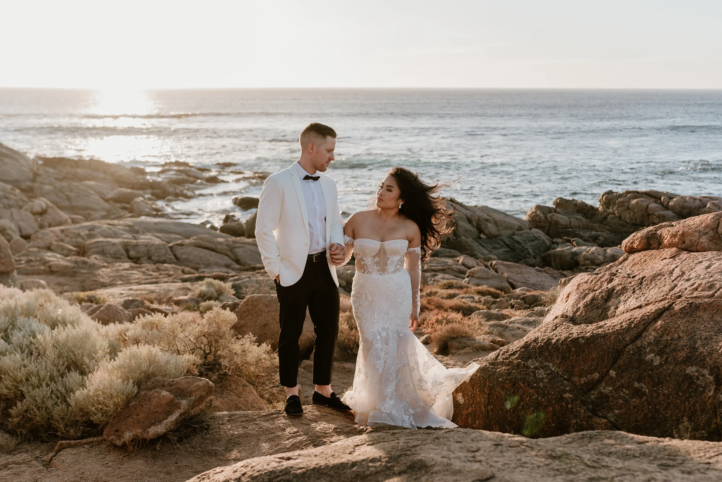 Sunlit candid portrait of the newlywed couple standing on the rocks at Smiths Beach in Yallingup