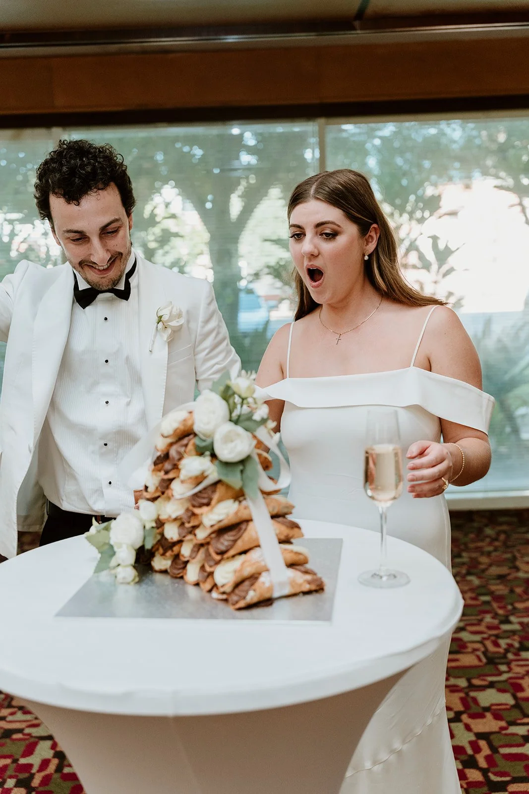 Bride and groom looking at a cake at their wedding reception, with a glass of champagne on the table.