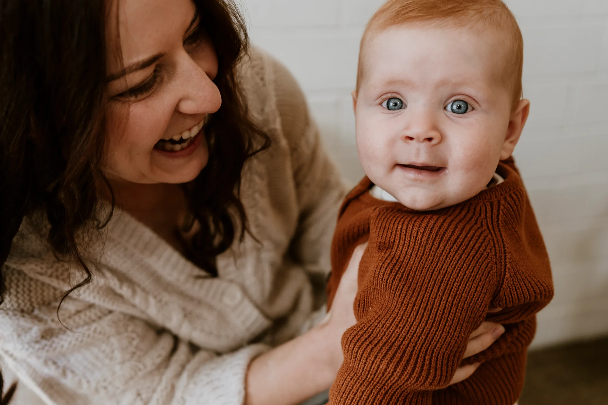 A loving moment between mother and baby, both wearing coordinated warm colours and knit textures