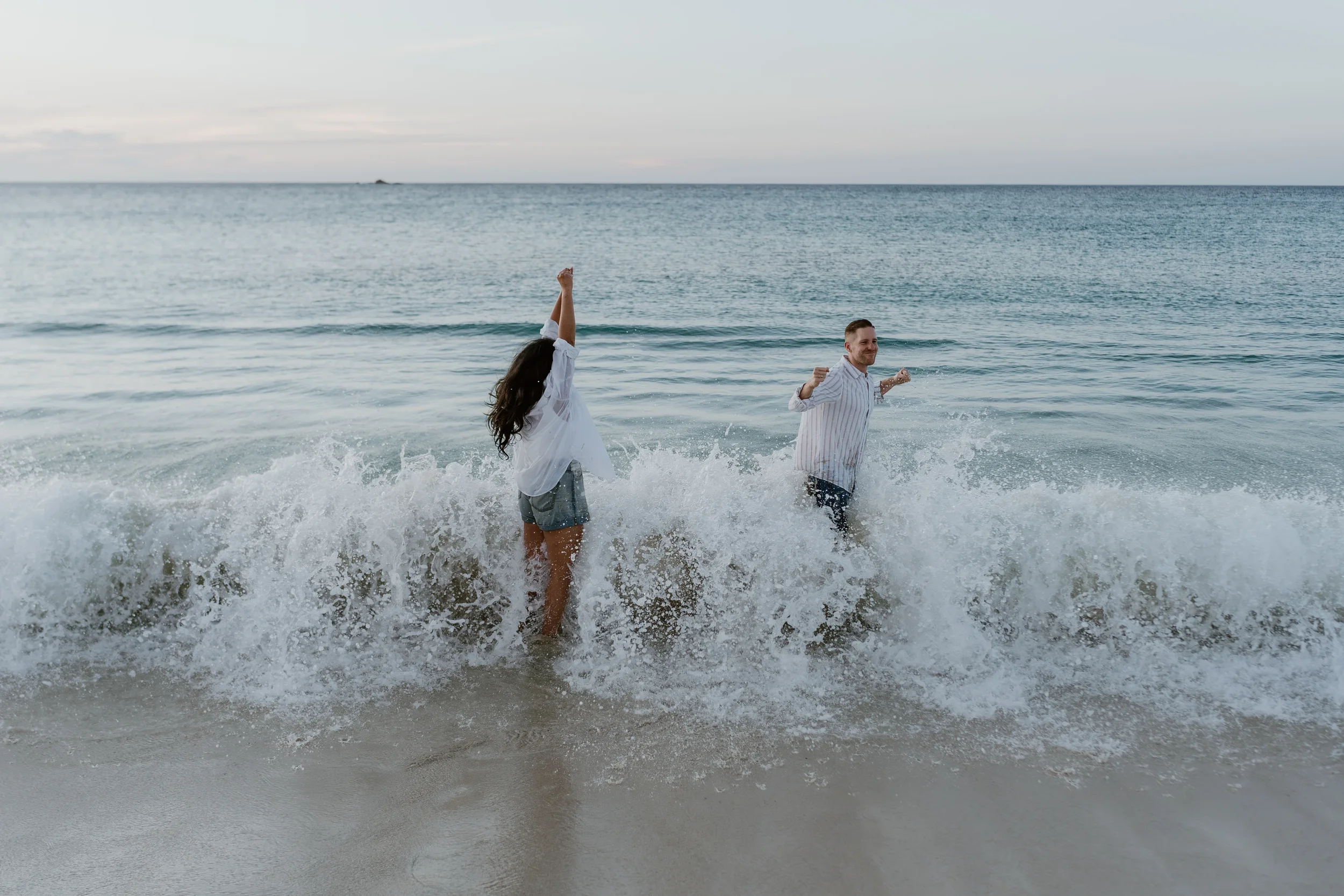 A man and a woman playing joyfully in the ocean waves at the beach during daytime.