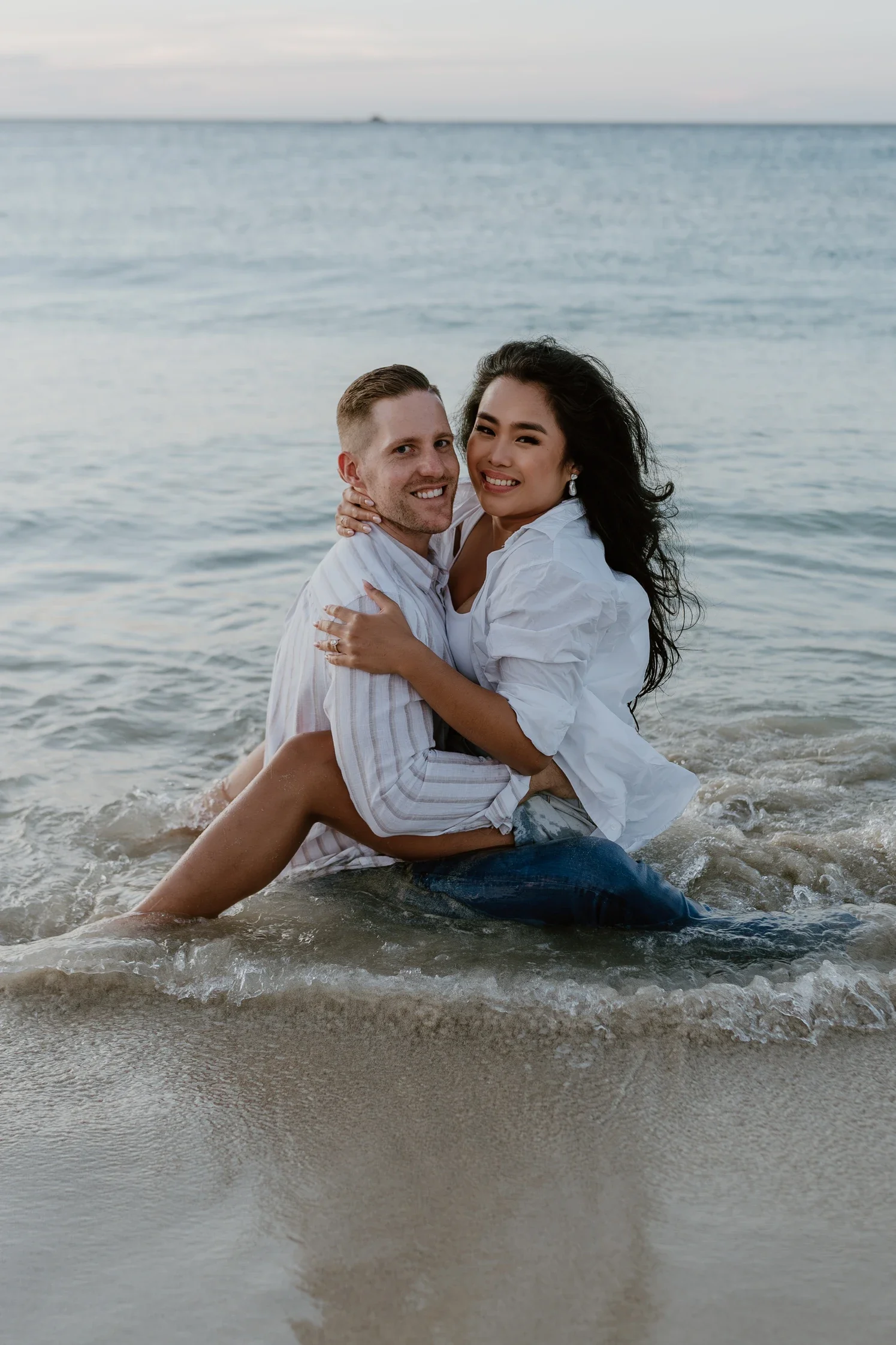 Kristelle and Joel embracing in the shallows of the calm water during their couple's portrait photography session at the beach