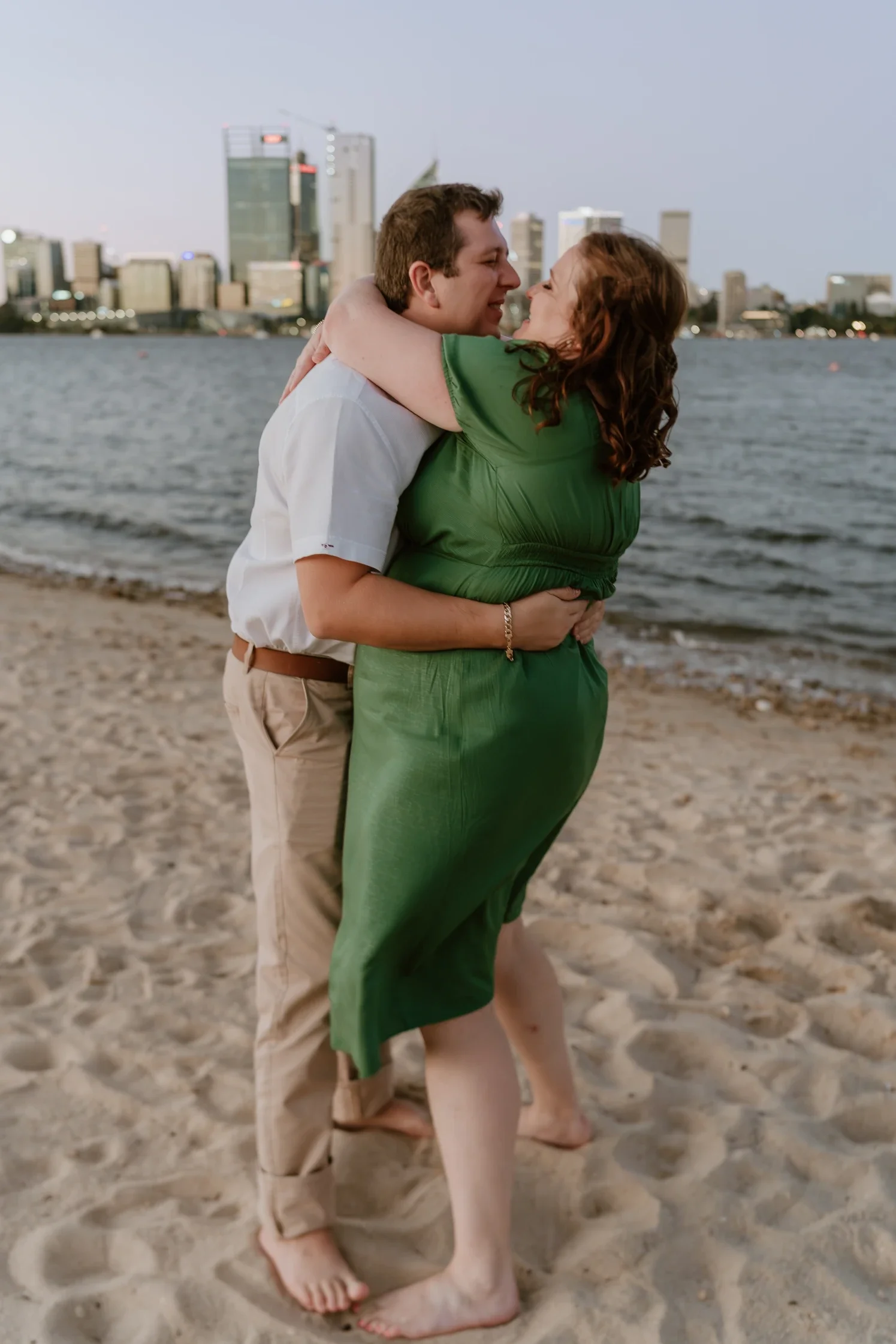 Couple embracing after their engagement, with the Perth city skyline glowing behind them