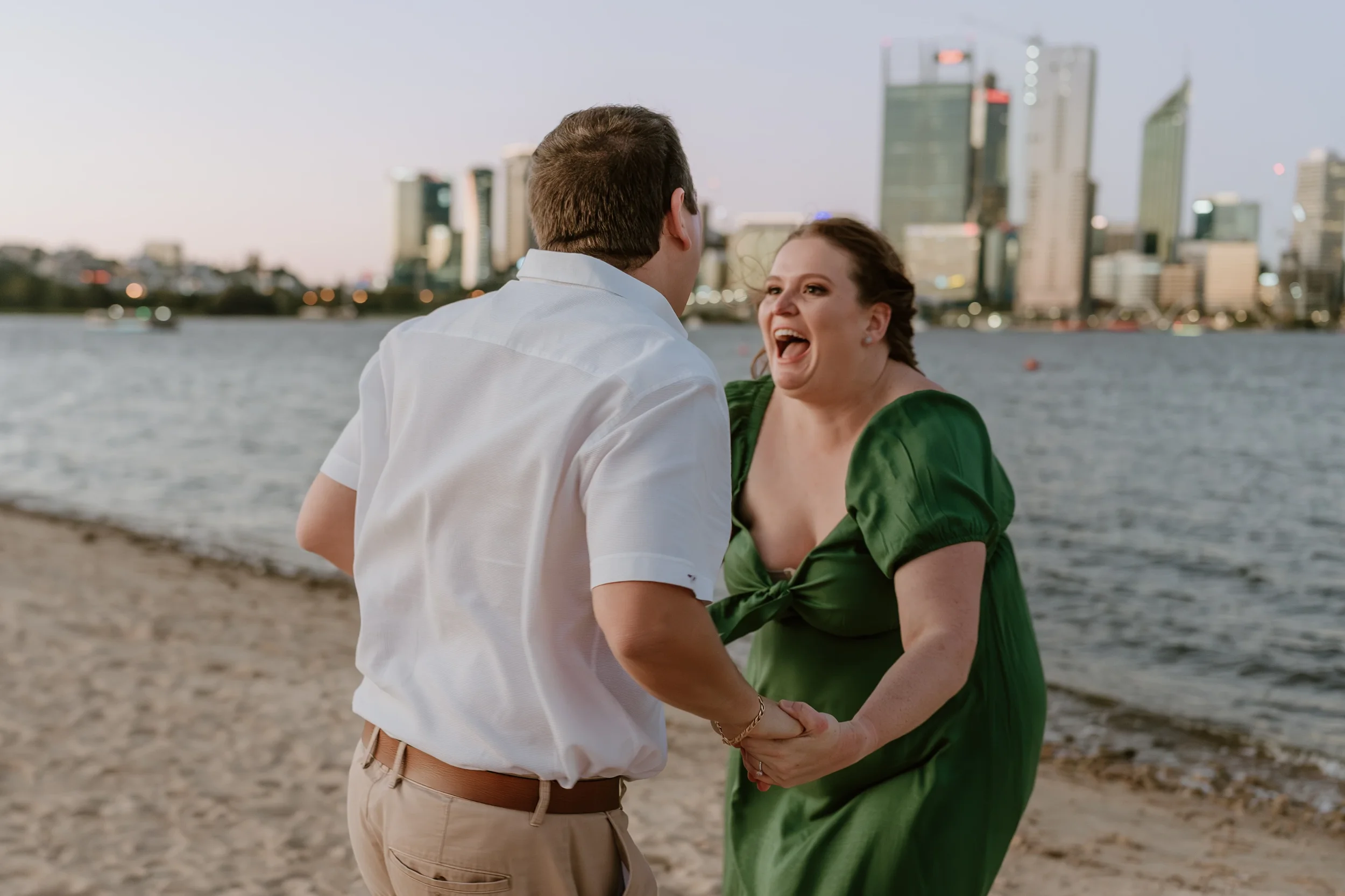 Candid moment as the newly engaged couple laughs in the soft light just after sunset on the banks of the Swan River in South Perth