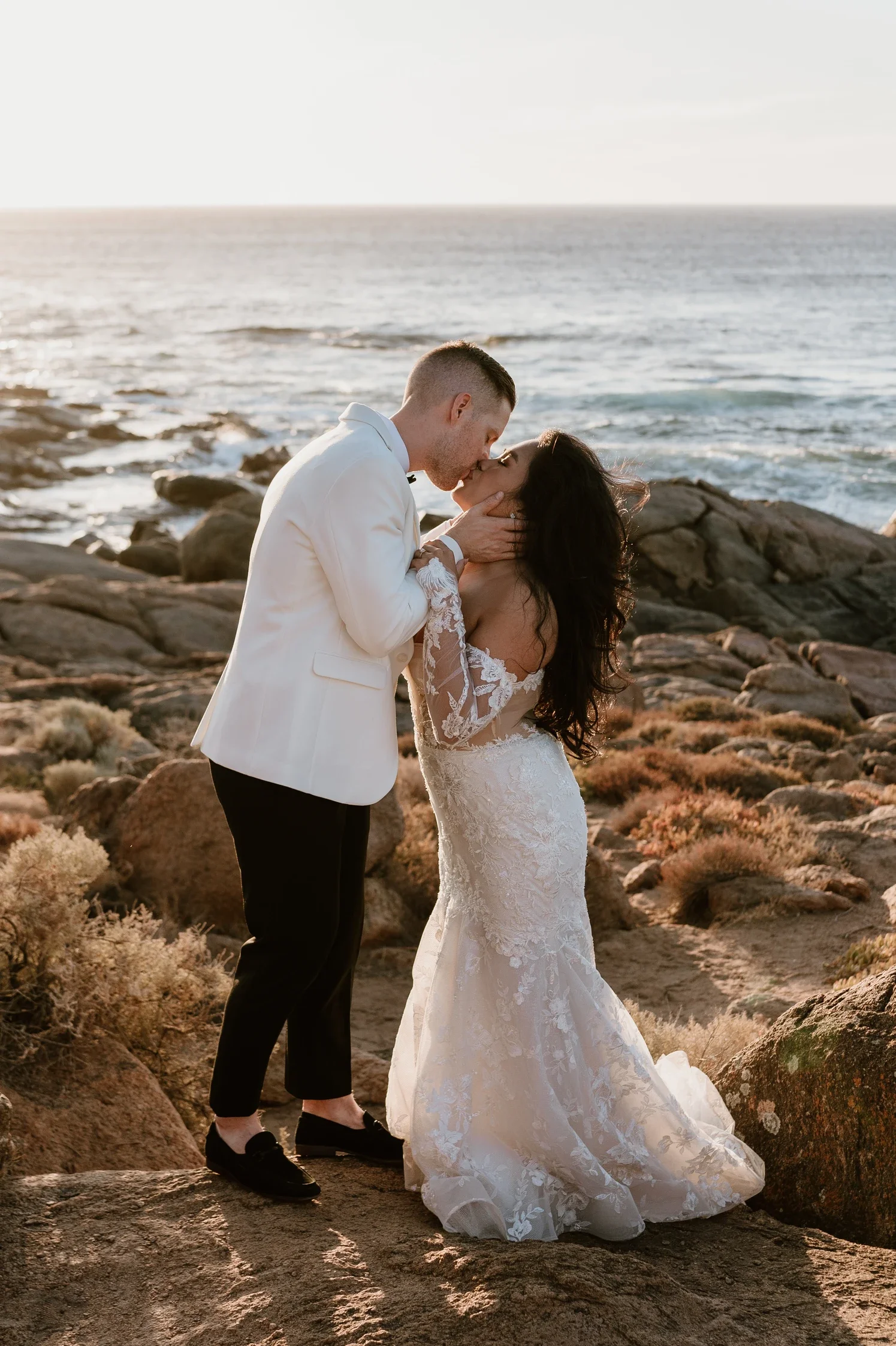 A sunlit portrait of the newlywed couple sharing a kiss on the rocks at Smiths Beach in Yallingup on their wedding day