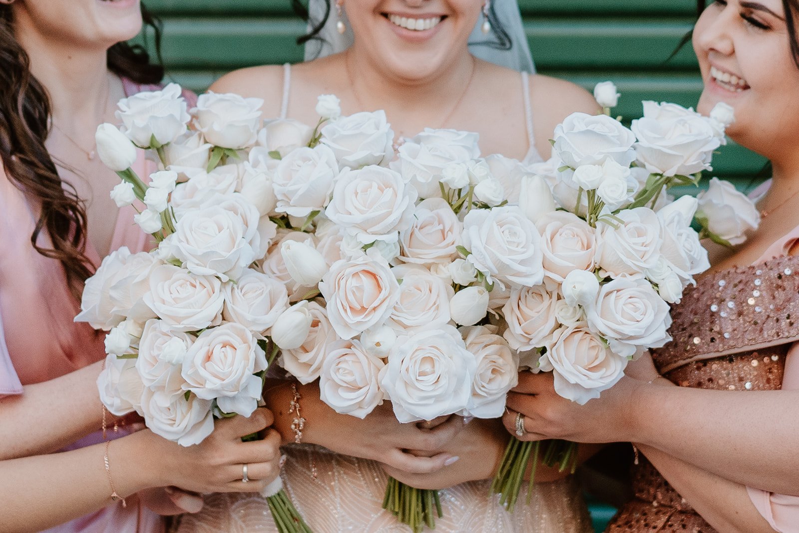 Three women holding a large bouquet of white roses at a celebration or event.