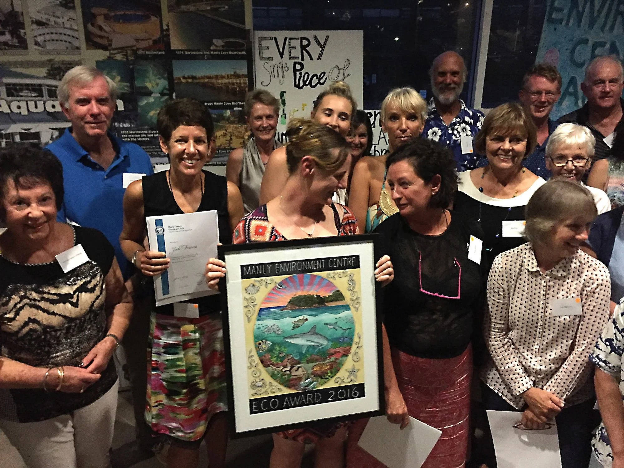 Group of people at an award ceremony holding a framed eco award poster that reads 'Manly Environment Centre Eco Award 2016'.