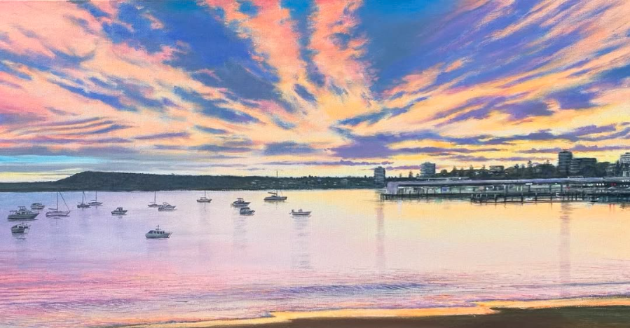 Sunset over a calm harbor with boats and a distant city skyline.