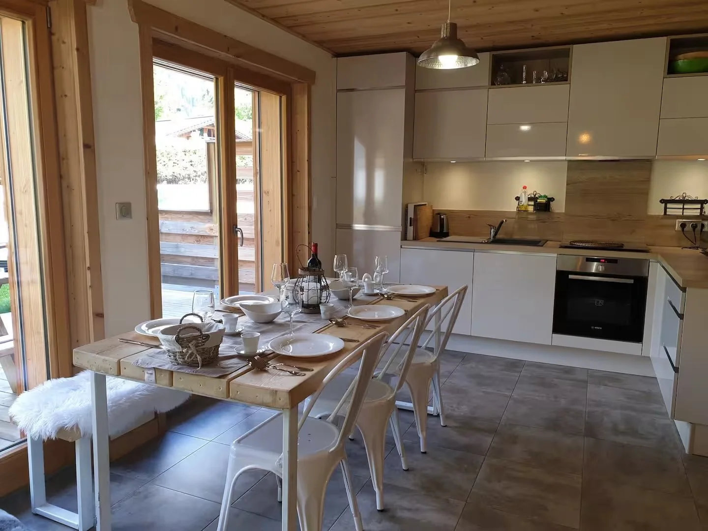 Dining table set for six in a modern kitchen with sliding glass doors leading outside, wood accents, and minimalist decor.