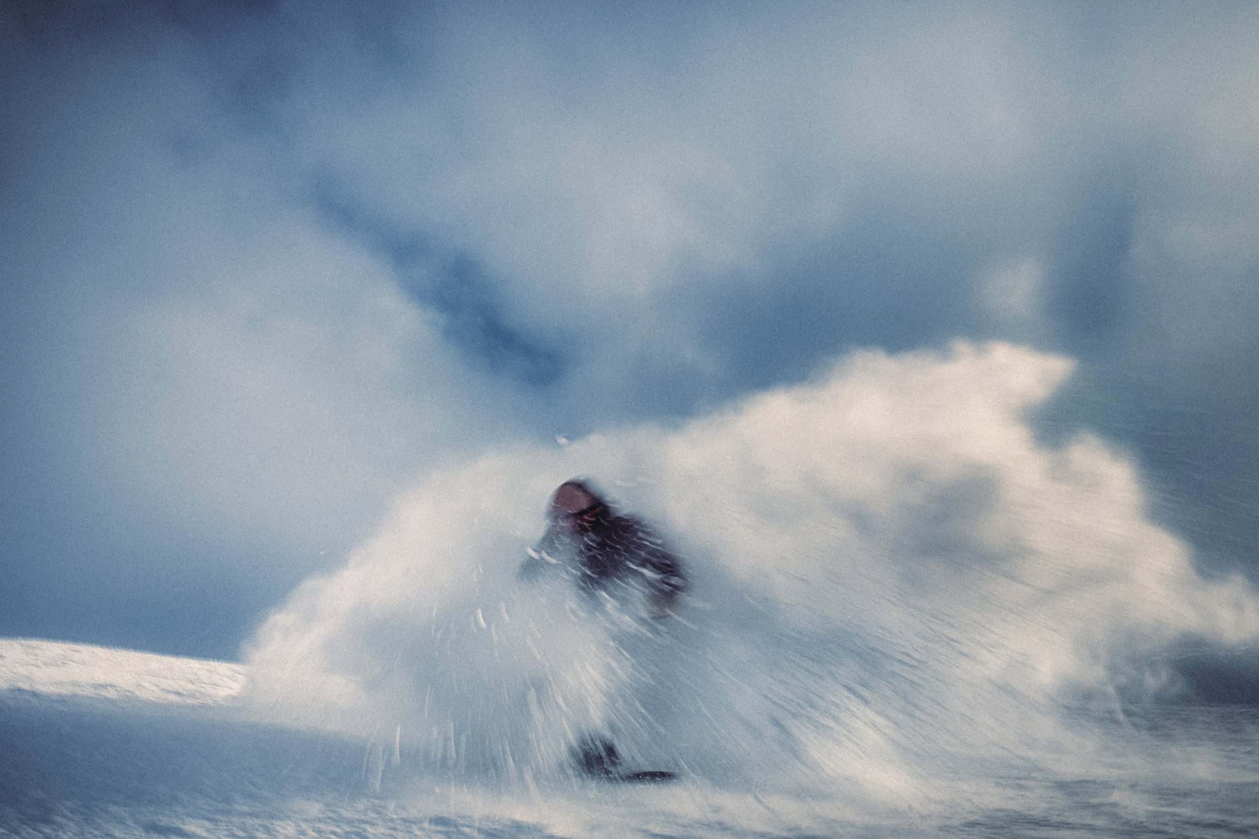 A snowboarder in a black jacket and helmet making a sharp turn on a snowy mountain slope, kicking up snow.