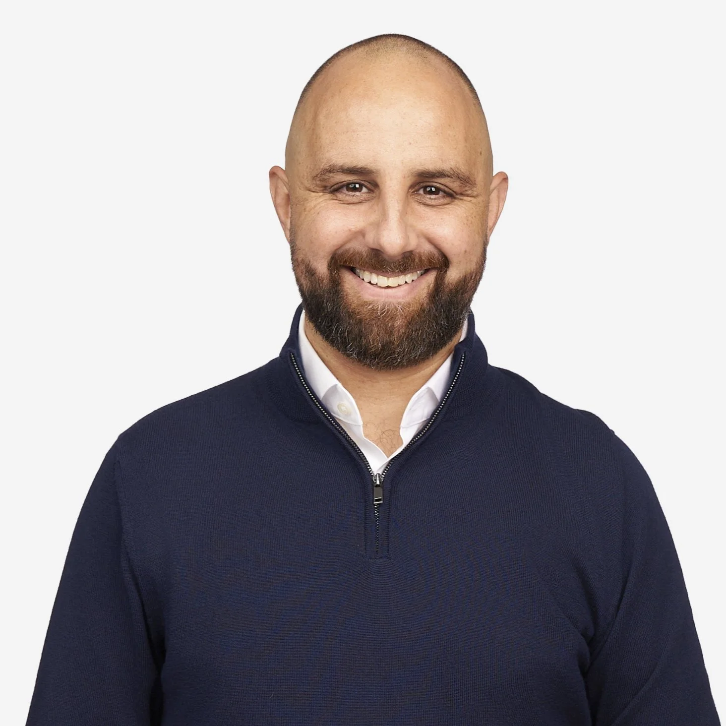 Smiling man with a beard and mustache, wearing a navy blue zip-up sweater over a white collared shirt, against a plain white background.