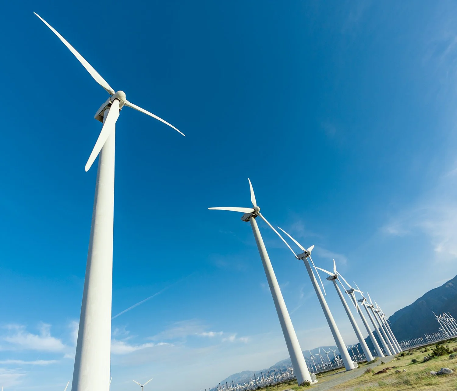A row of wind turbines in a green landscape under a clear blue sky.
