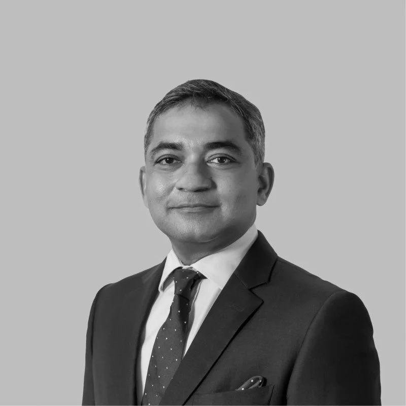 A black and white headshot of a man in a suit and tie, smiling slightly, against a plain background.