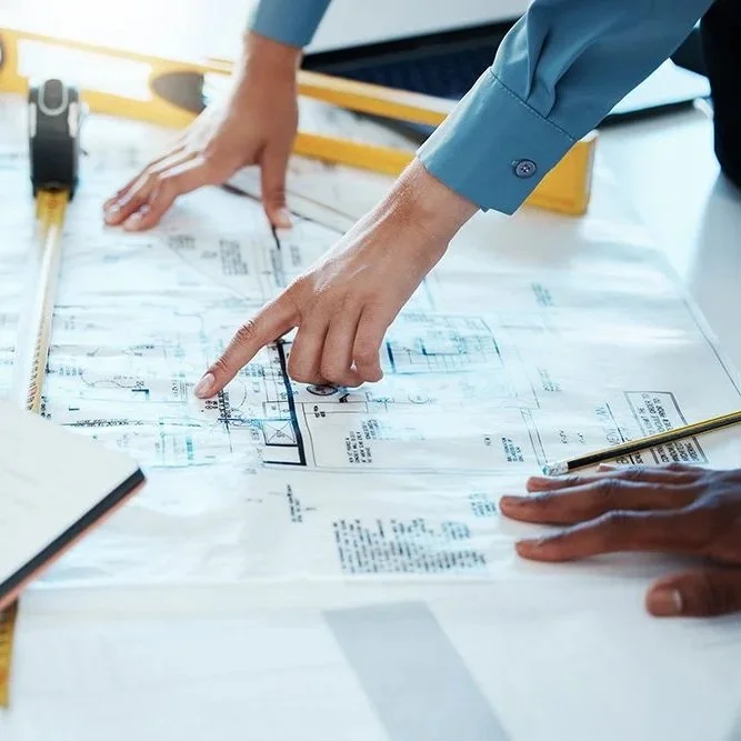 Two people examining architectural blueprints on a table, with a ruler and a pencil nearby.