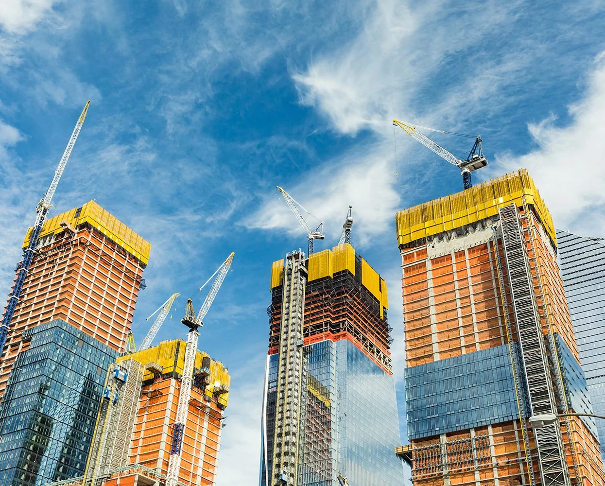 Several tall skyscrapers under construction with cranes on a blue sky.