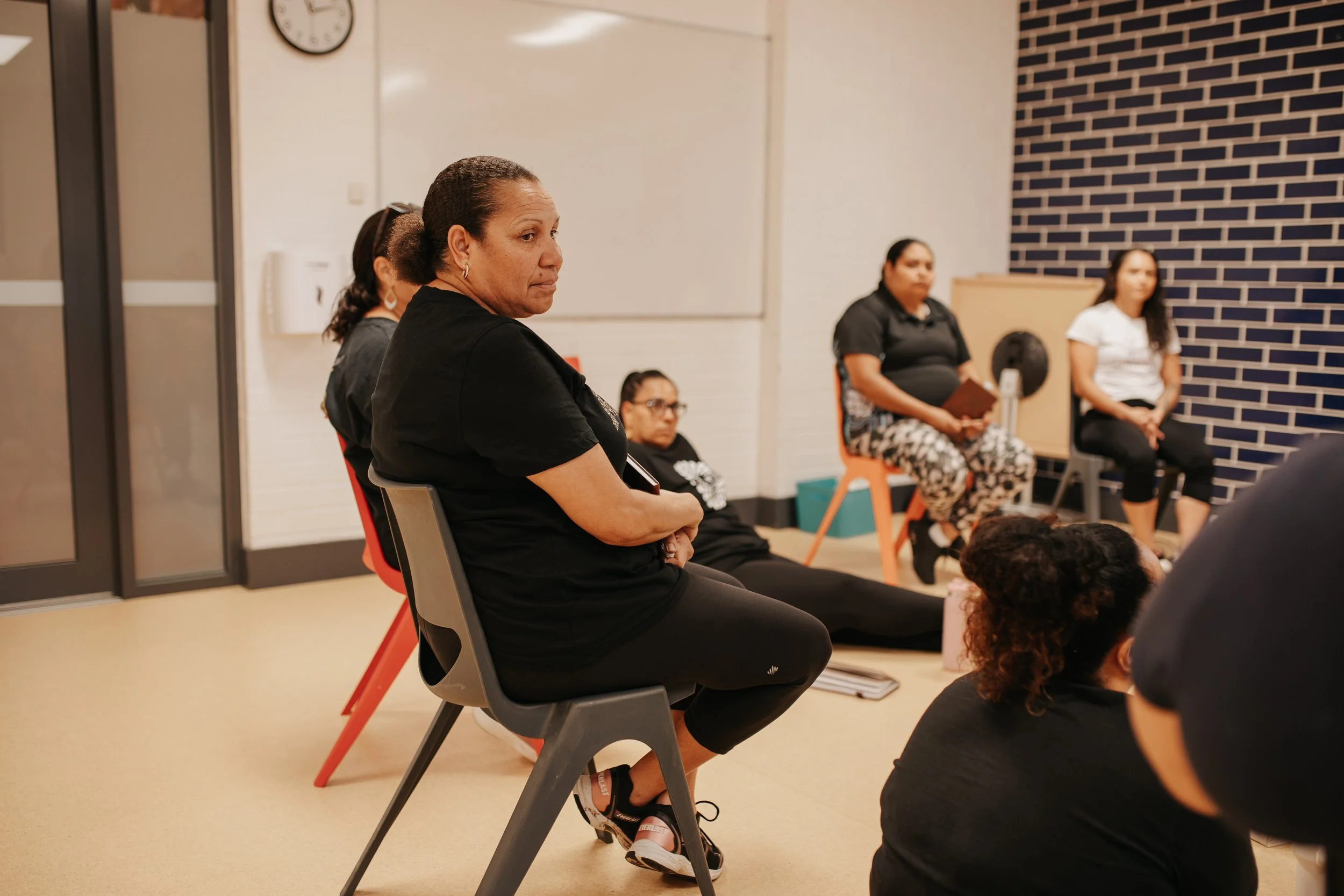 Women attending a group meeting or discussion in a room, seated and listening attentively.