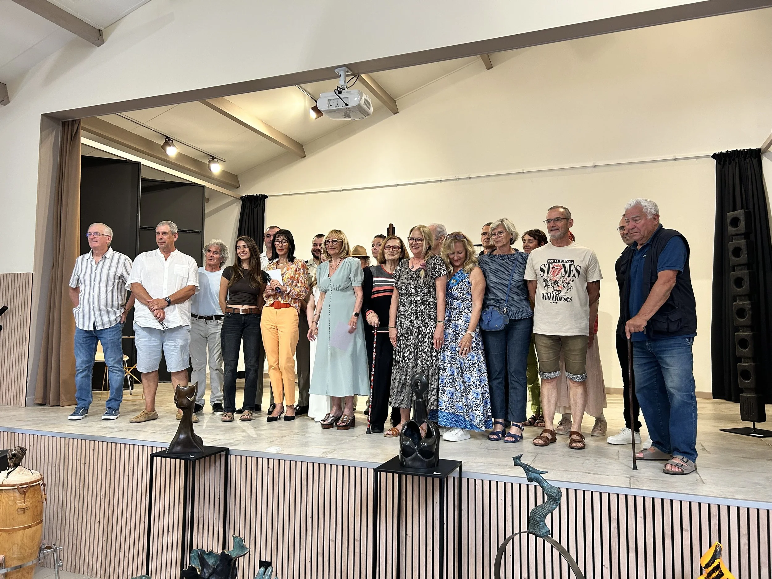 Groupe de personnes sur scène lors d'un événement, devant un mur blanc, avec des sculptures en bas.