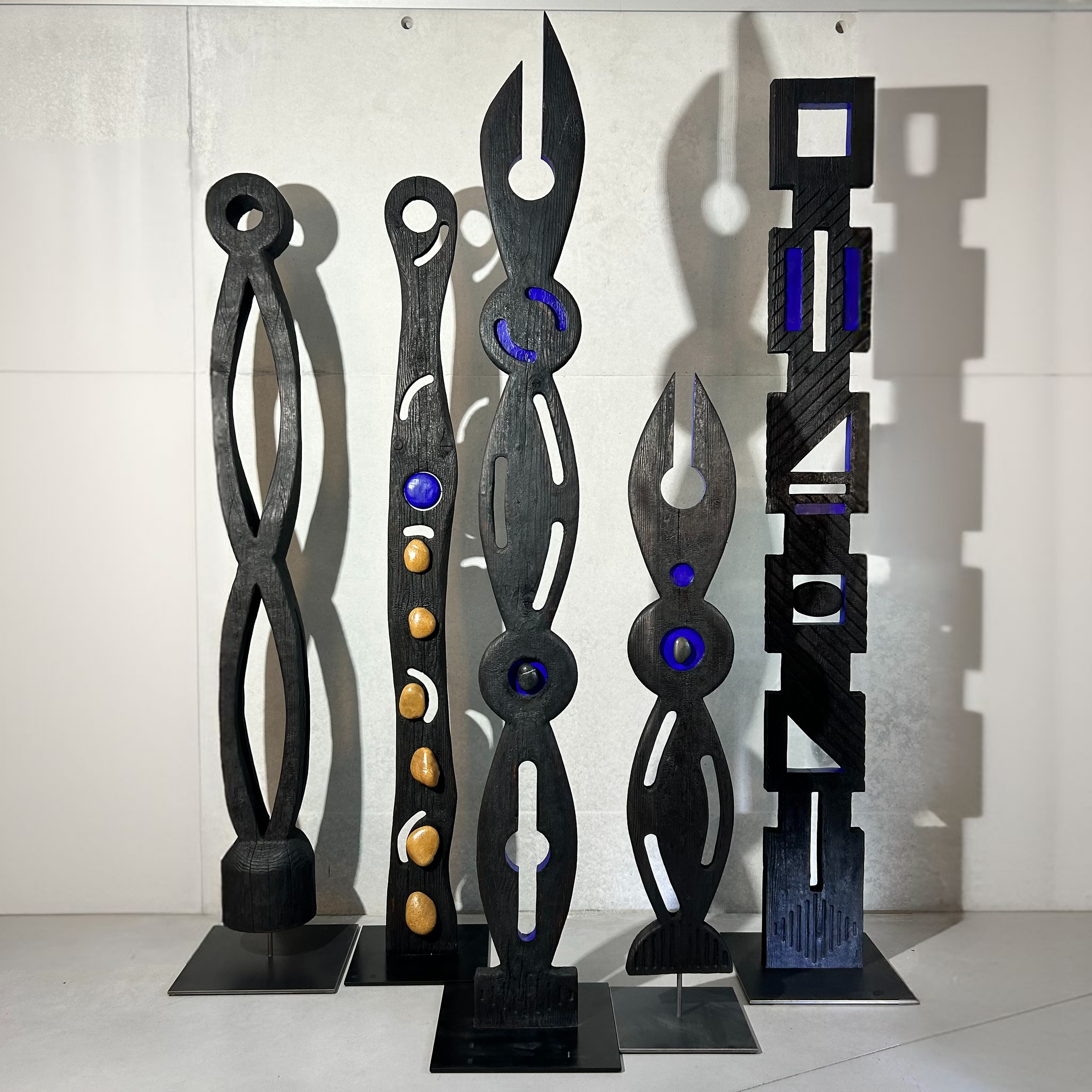 Sculptures en bois abstraites noires avec des accents colorés, exposées sur des socles métalliques.