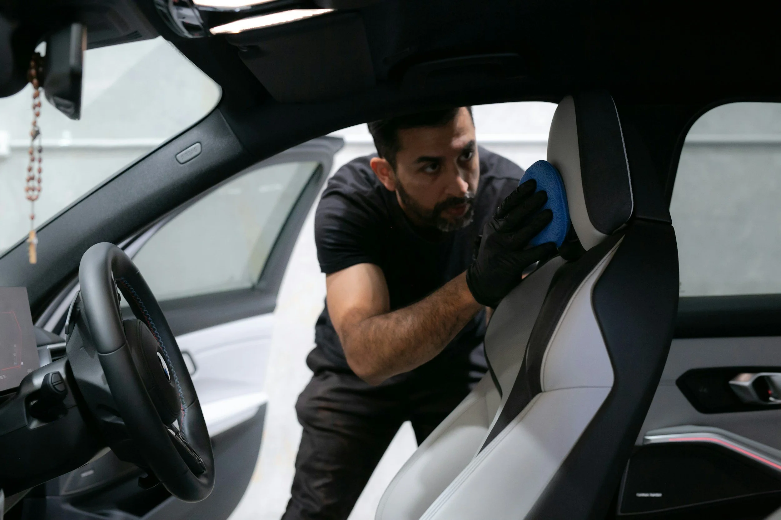 A man cleaning the interior of a car, focusing on the headrest with a blue cloth, inside a modern vehicle.