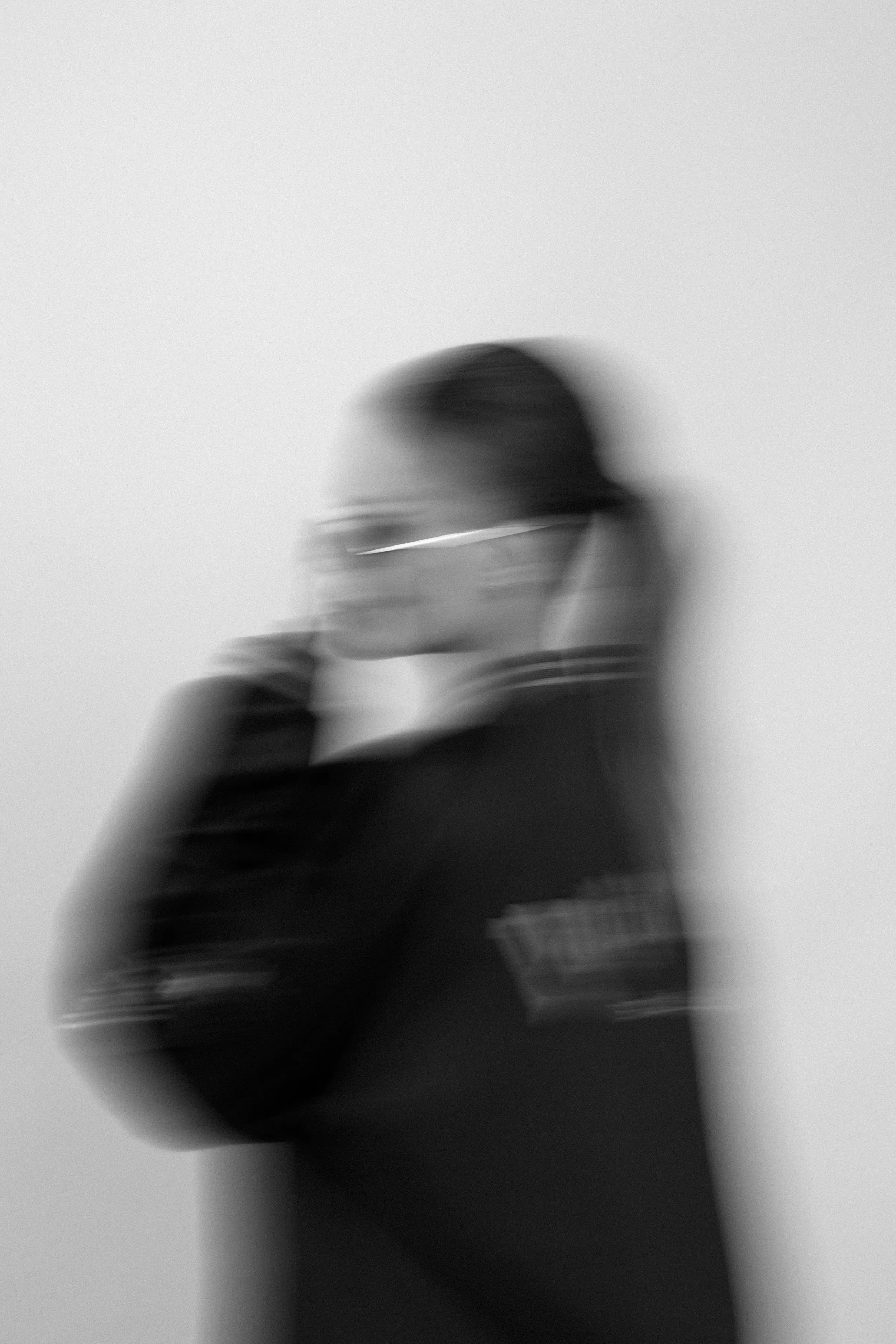 A blurry black-and-white photo of a person wearing glasses with arms crossed, against a plain light background.