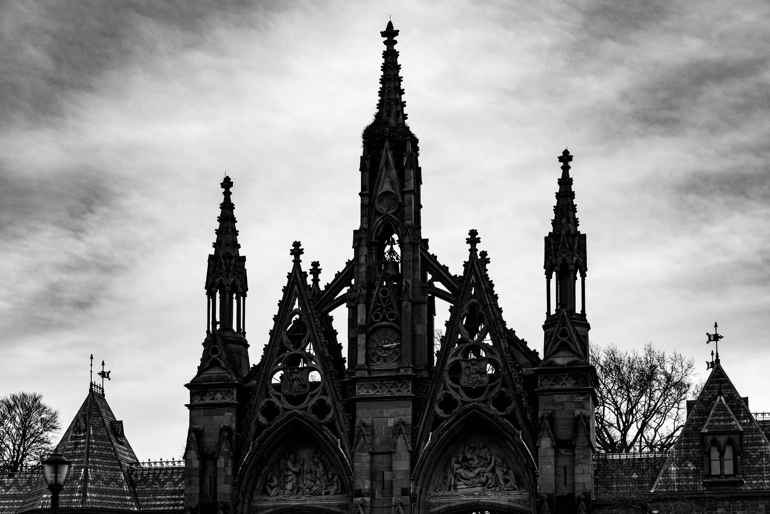 A black and white photo of a Gothic-style church with tall spires and detailed stone carvings, set against a cloudy sky.