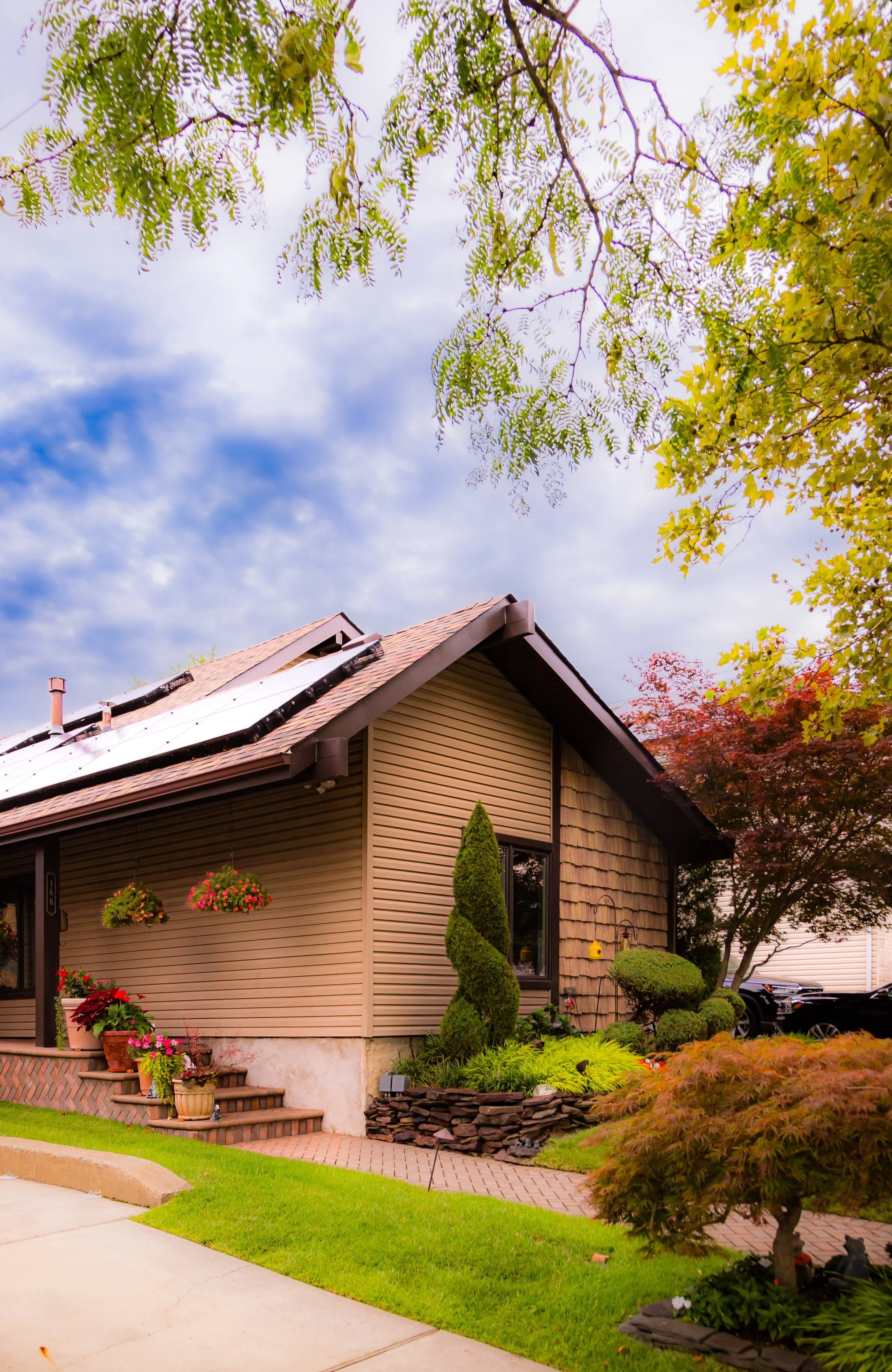 A house with a sloped roof and solar panels, surrounded by a well-maintained garden with plants, trees, and flowers.