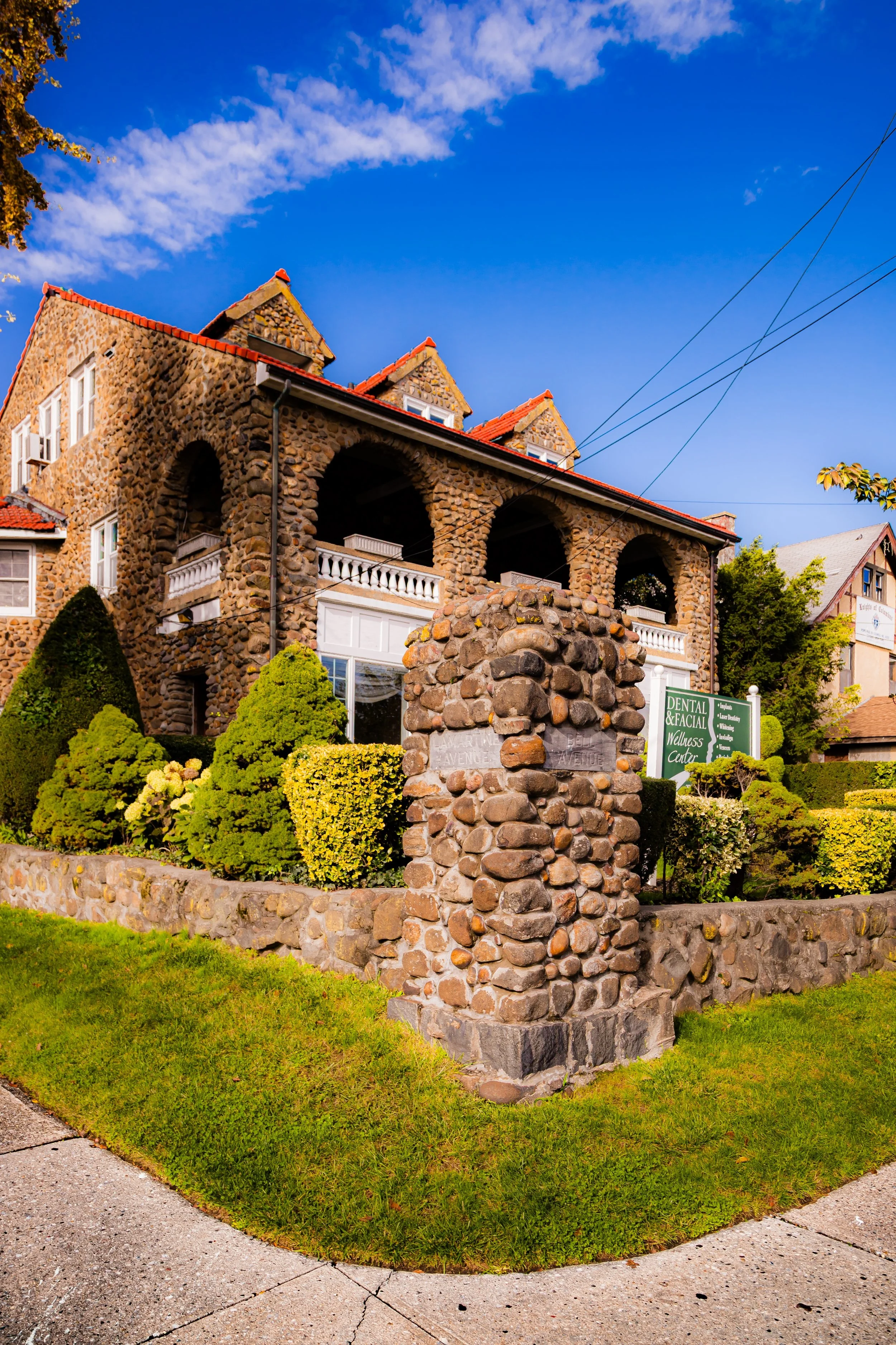 Stone building with manicured bushes in front and a sign for a dental and facial wellness center.