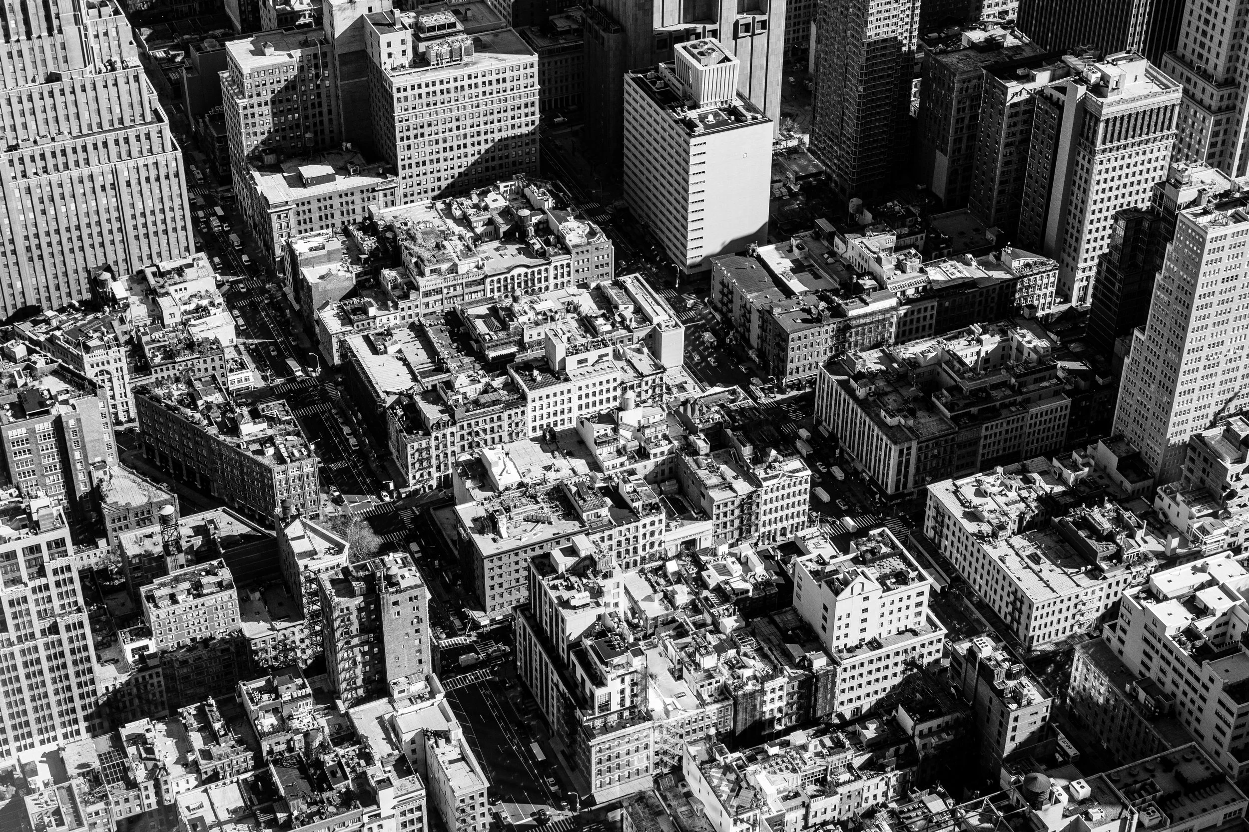 A black and white aerial view of a dense cityscape with numerous tall buildings, streets, and rooftops.