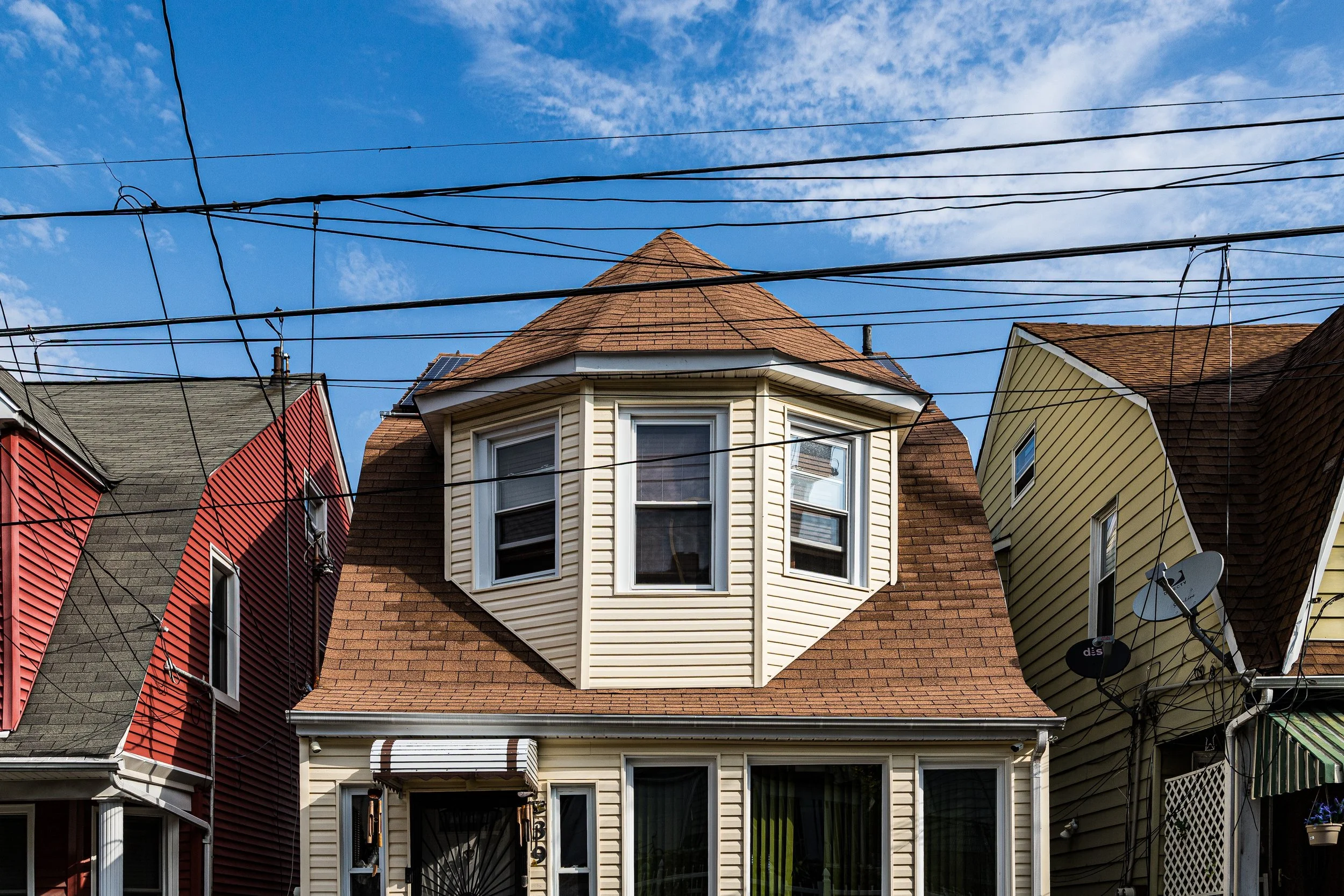A row of houses with different colored exteriors, with black power lines and a blue sky with scattered clouds overhead.