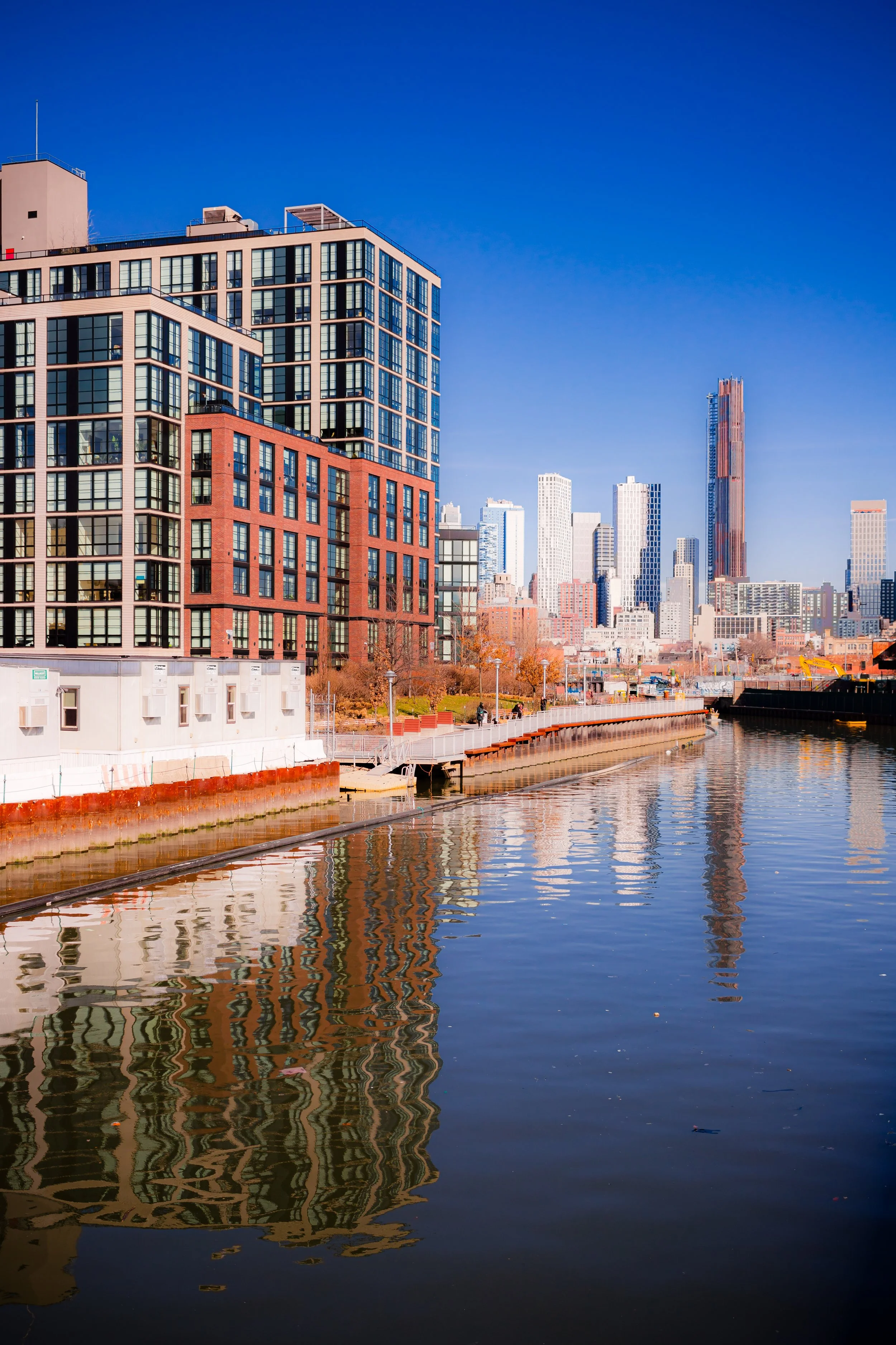 City skyline with modern high-rise buildings along a river under a clear blue sky.