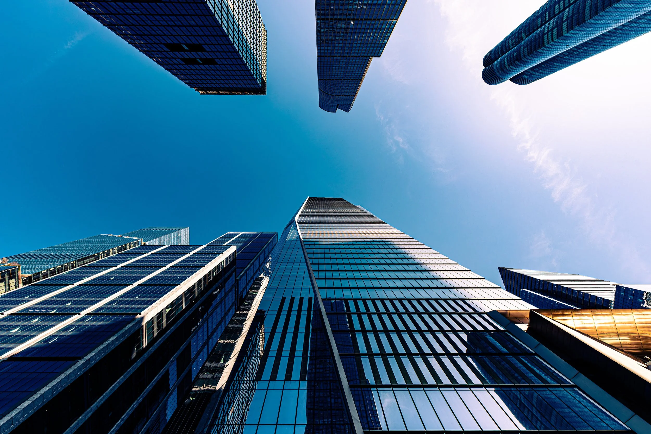 Looking up at tall modern skyscrapers with glass facades against a blue sky.