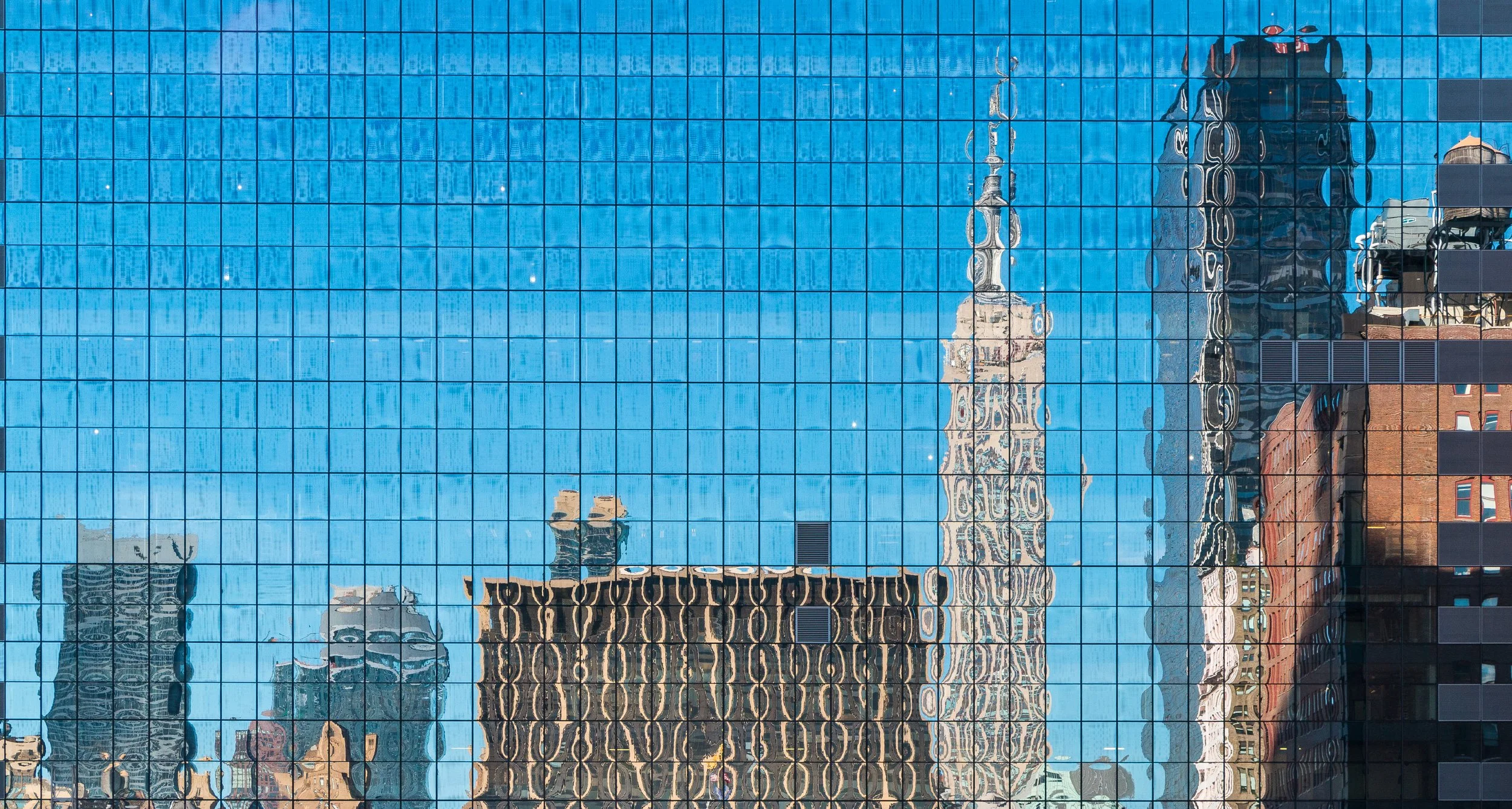 Reflections of surrounding buildings and blue sky on a grid-patterned glass skyscraper.
